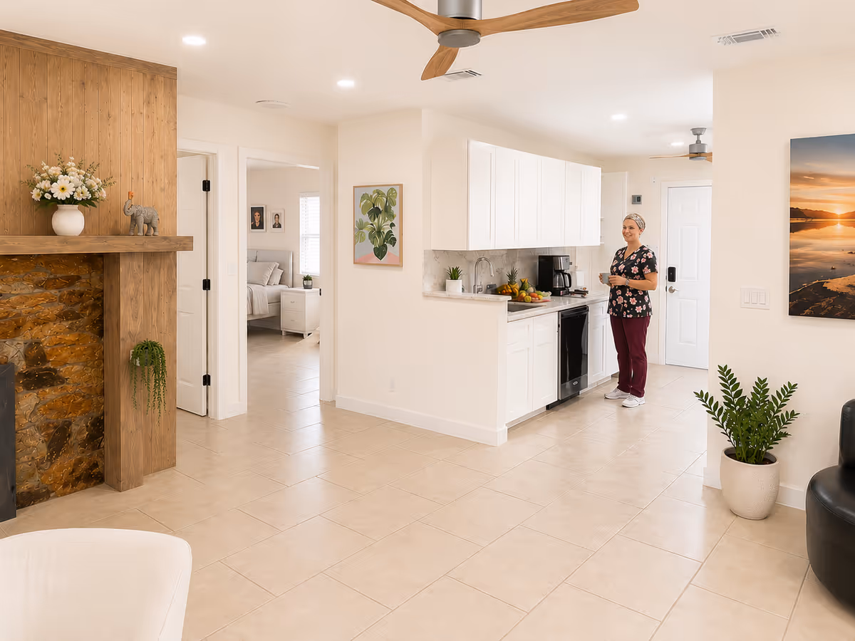 Bright open kitchen and living area with a staff member near white cabinets.