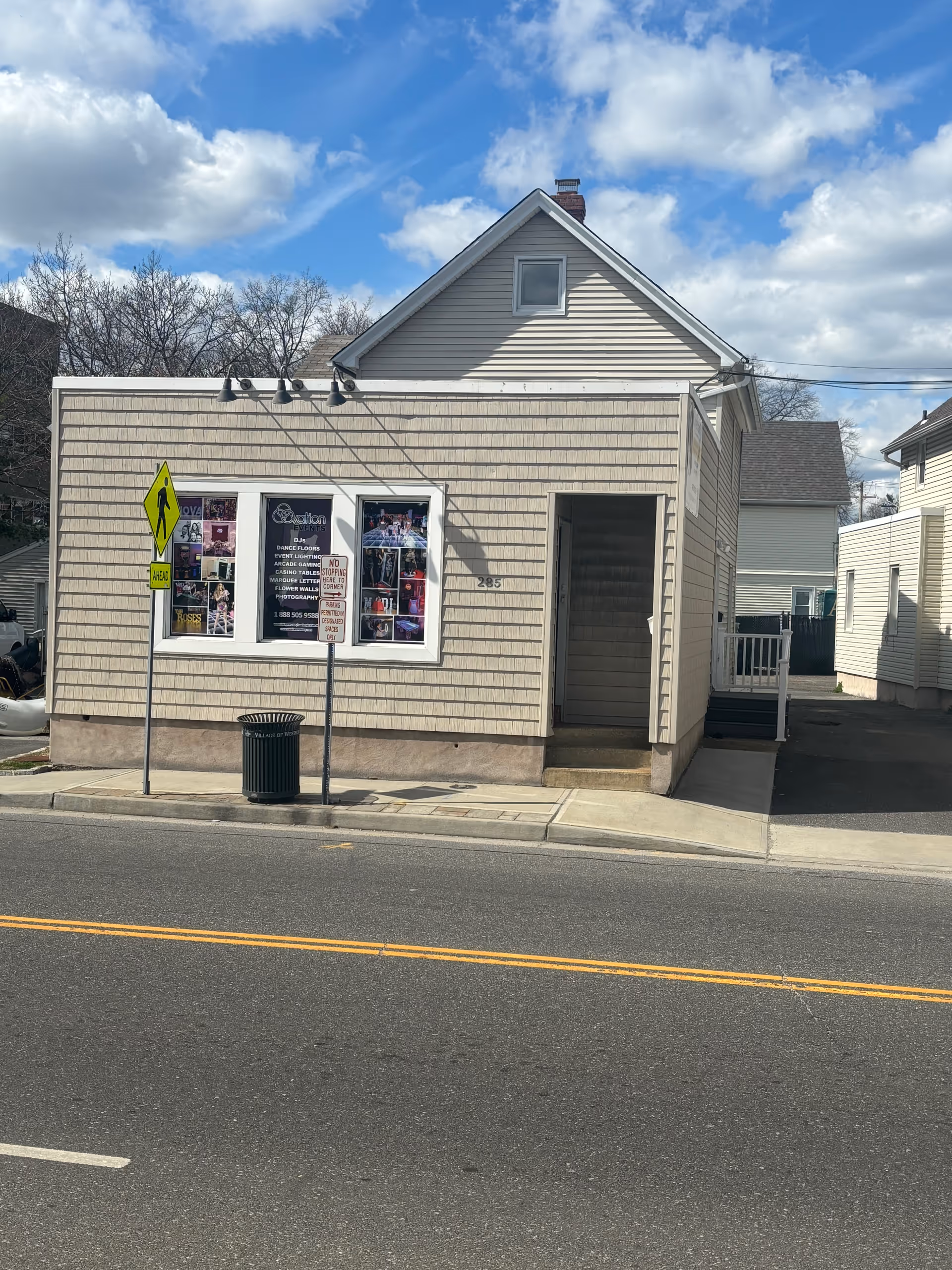 Small beige storefront building with posters in a front window and a sidewalk along the street.