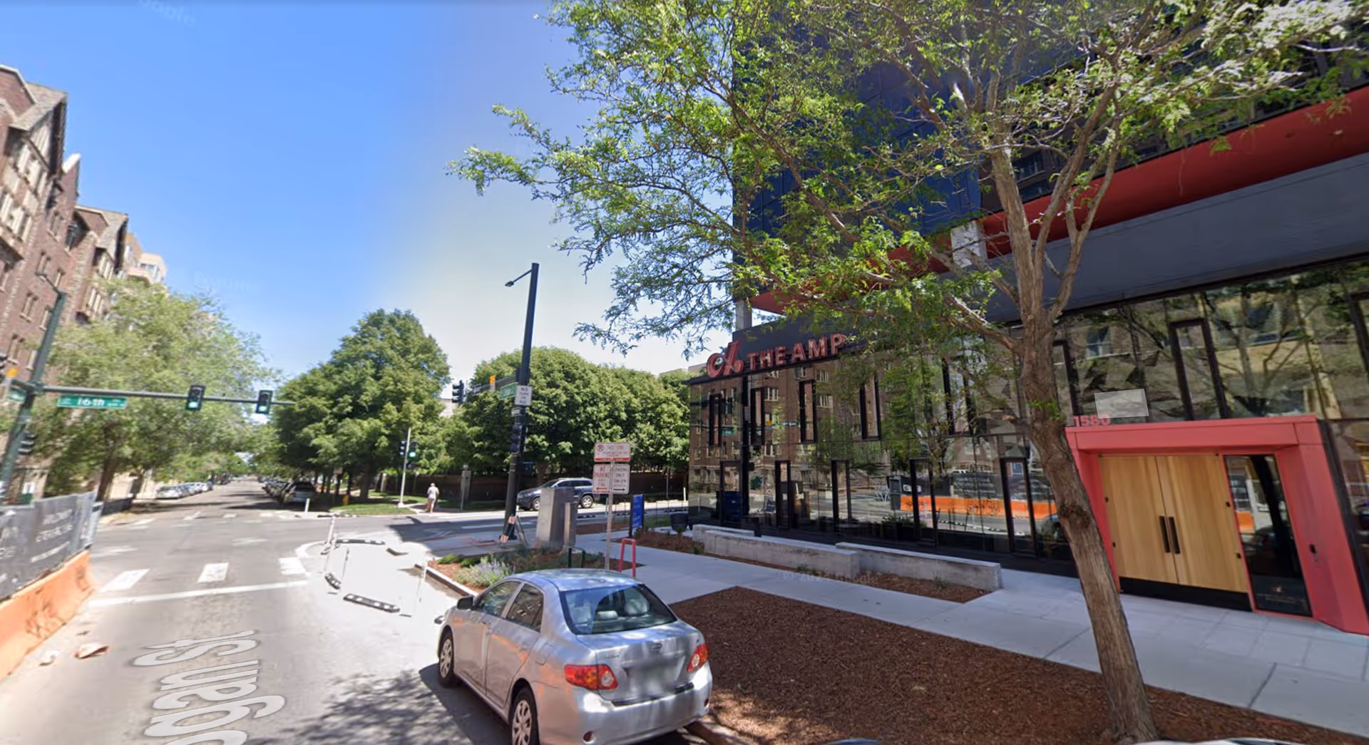 Urban street view with a modern building entrance, trees, and a parked car.