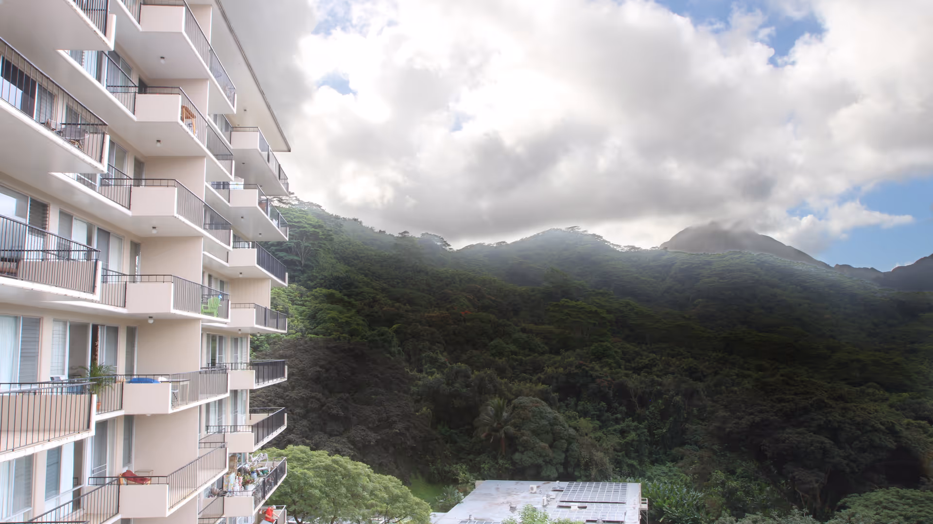 Multi-story residential building with balconies overlooking a lush, forested mountainside.