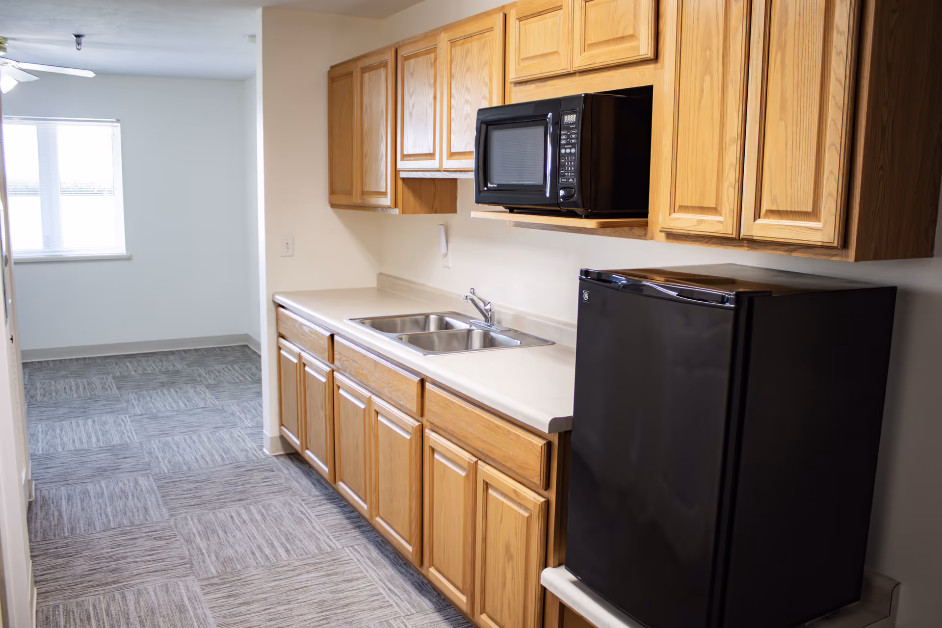 Wood kitchen cabinets, sink, microwave, and black refrigerator in Stonebridge Suites Onawa.