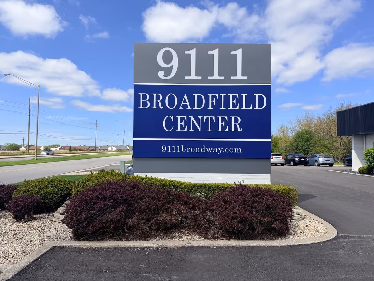 Large exterior sign for 9111 Broadfield Center with landscaping and a parking lot.
