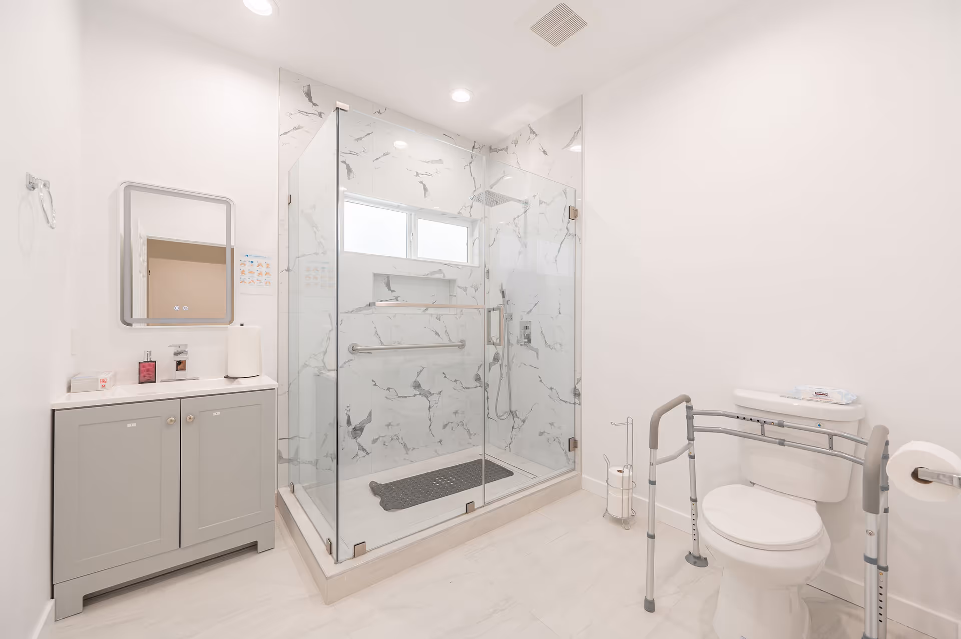 Bright bathroom with glass-enclosed shower, sink vanity, and toilet with grab bars.