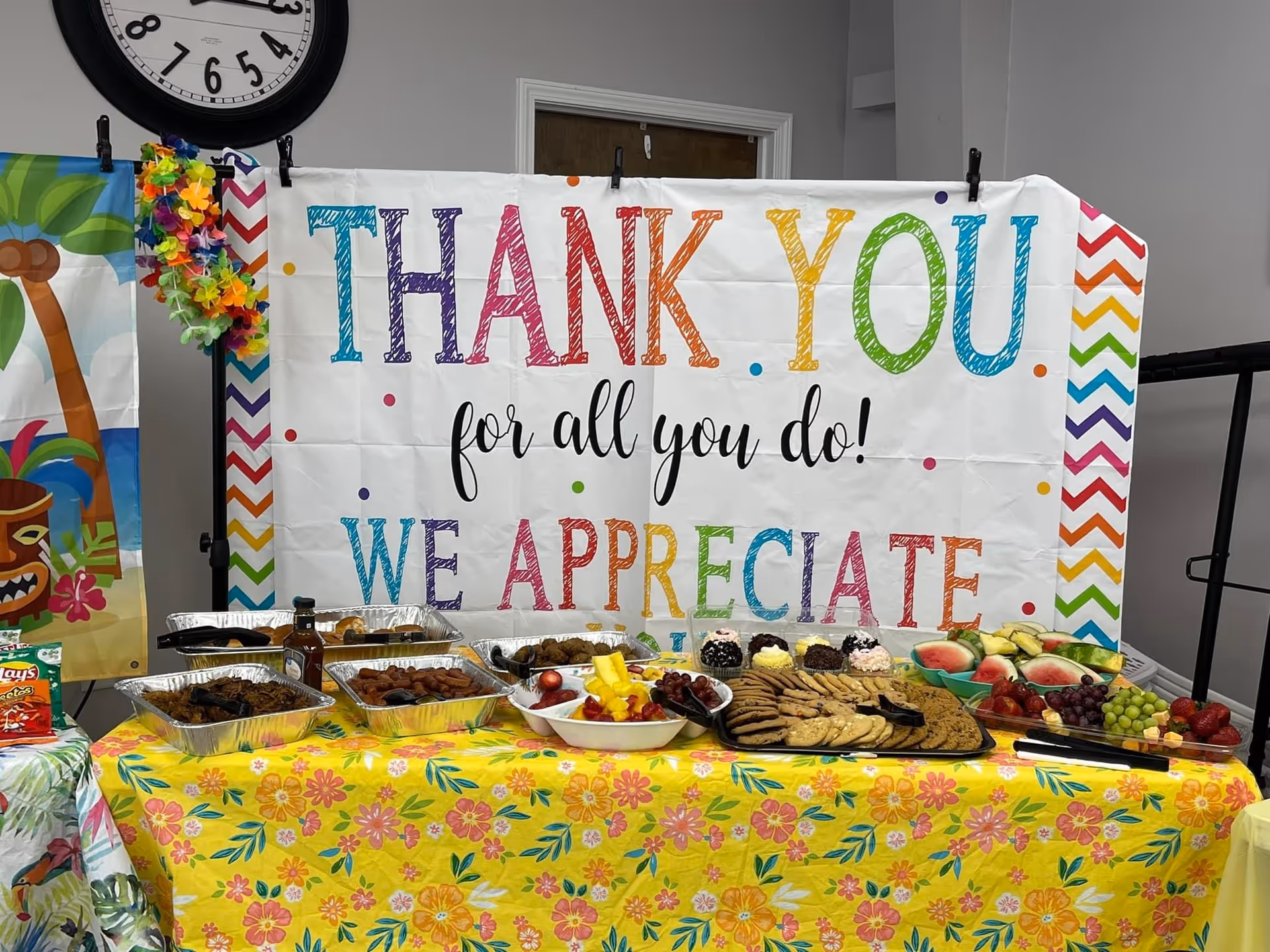 Colorful banner reads 'THANK YOU' above a long table of food indoors.