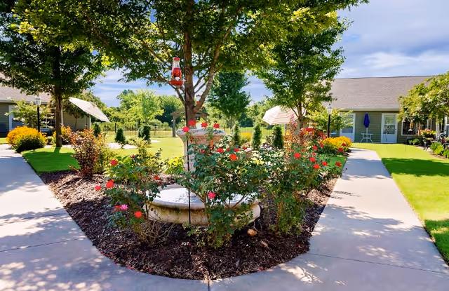 Sunlit courtyard of Adams County Nursing Center with rose garden, trees, and walkway.