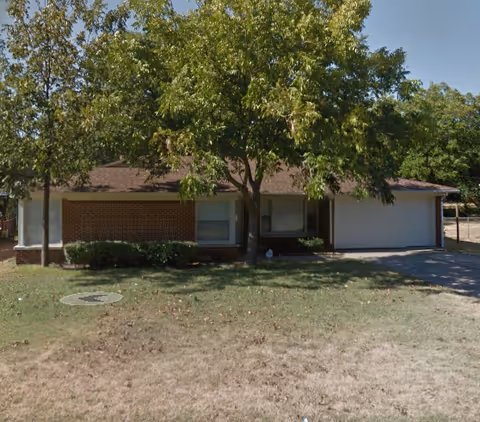 Front view of a single-story senior living building with trees and driveway.