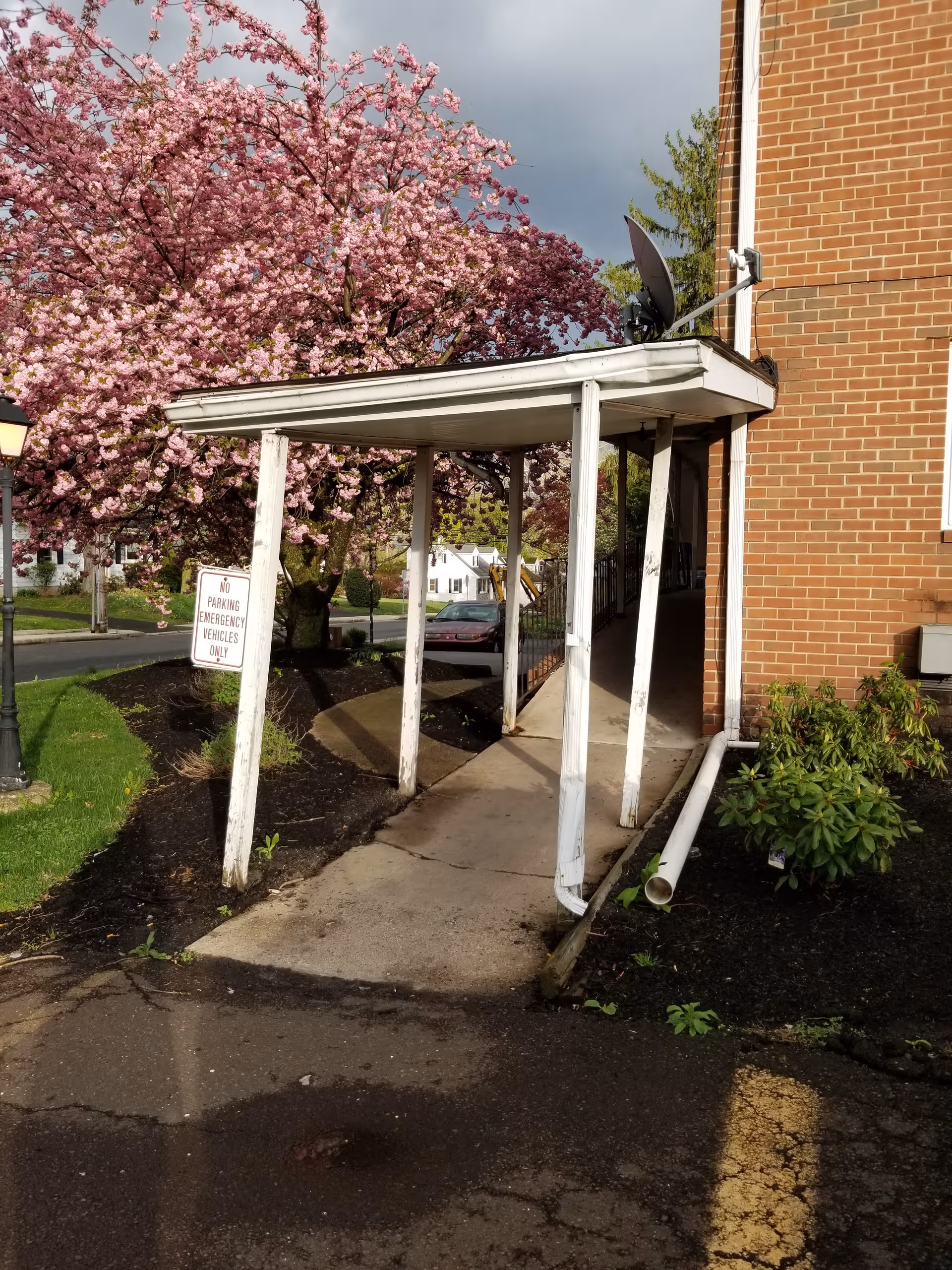 Brick senior living building exterior with a white canopy walkway and pink blossoms.