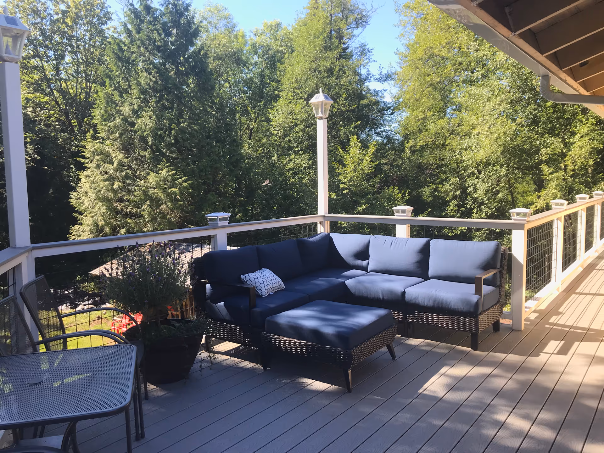 A wooden outdoor deck with blue cushioned lounge seating and surrounding trees.