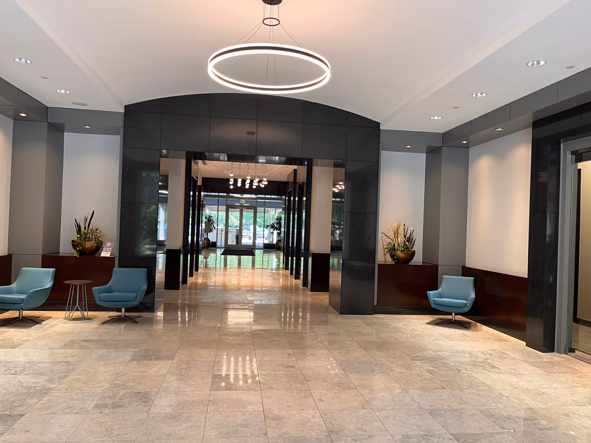 A modern hotel-like lobby with marble floors, blue chairs, and a doorway to outdoors.