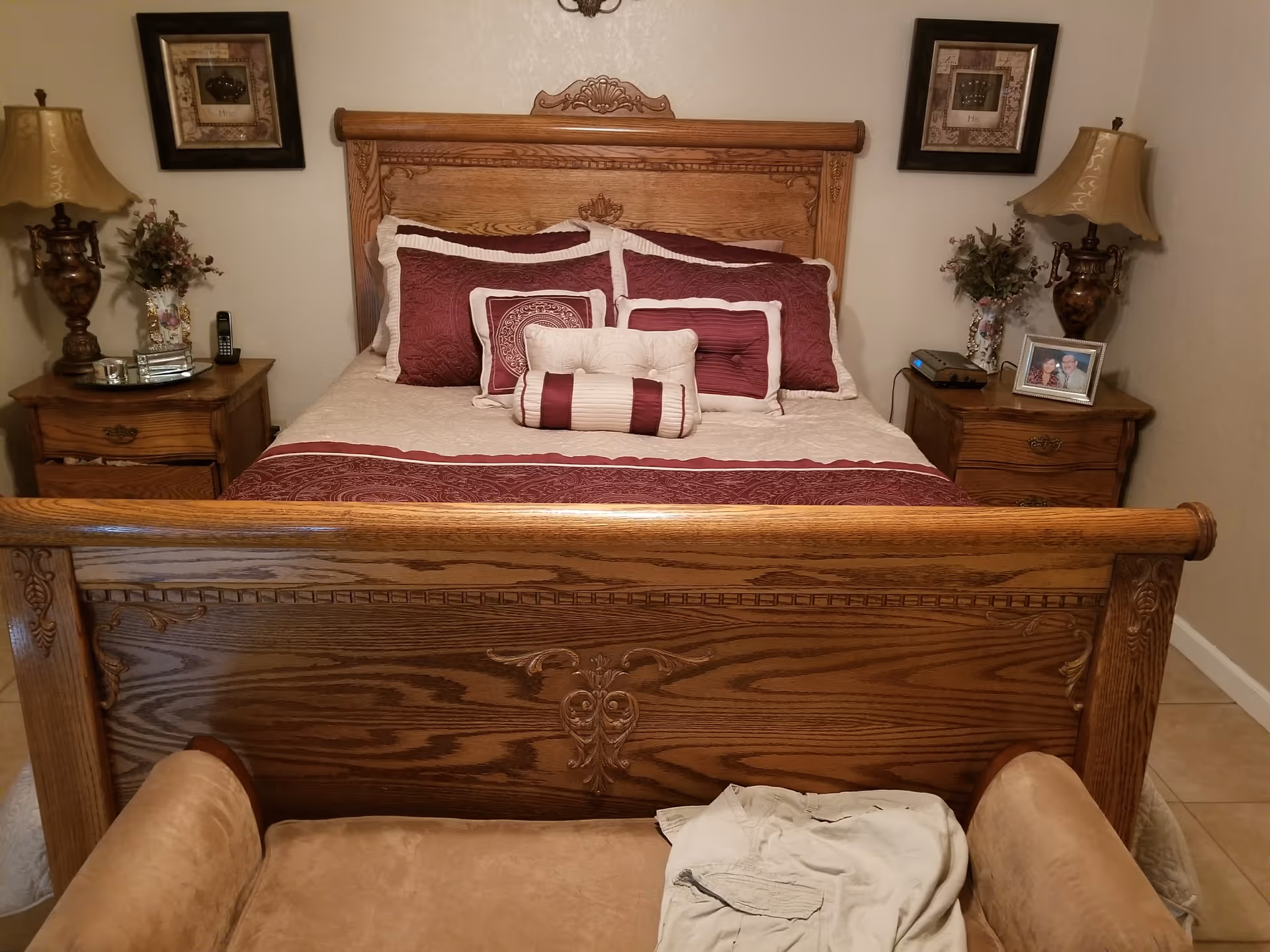 A wooden bed with burgundy bedding, matching nightstands, lamps, and decorative framed art.