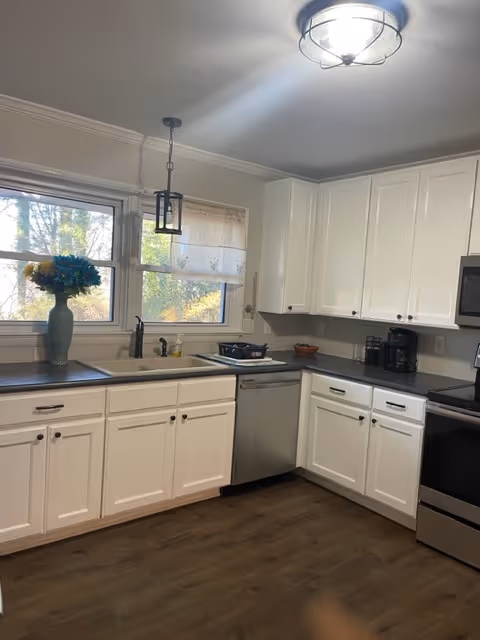 White kitchen with cabinets, stainless appliances, sink, and a vase by the window.