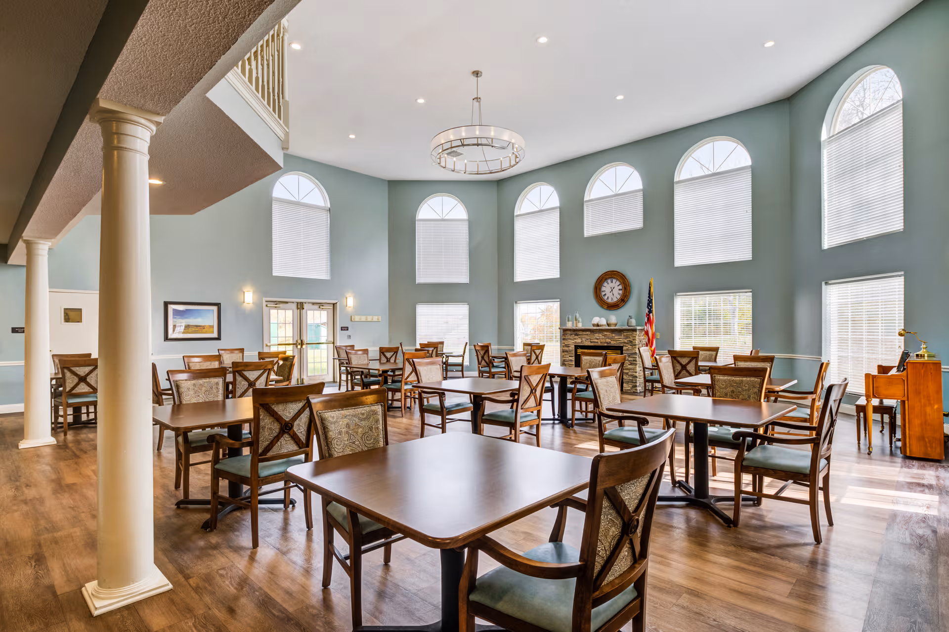 Spacious senior living dining room with multiple tables, chairs, and arched windows.