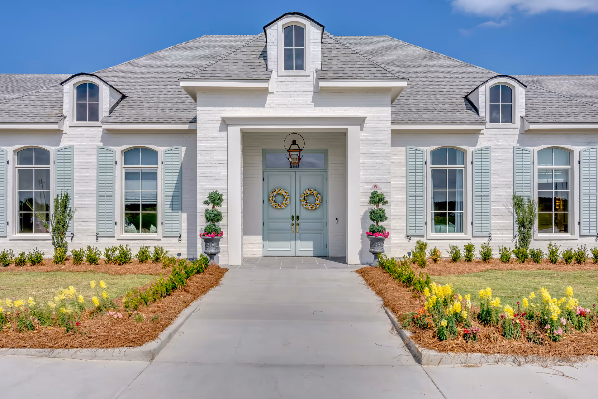 White brick senior living facility exterior with mint-green doors and flower planters.