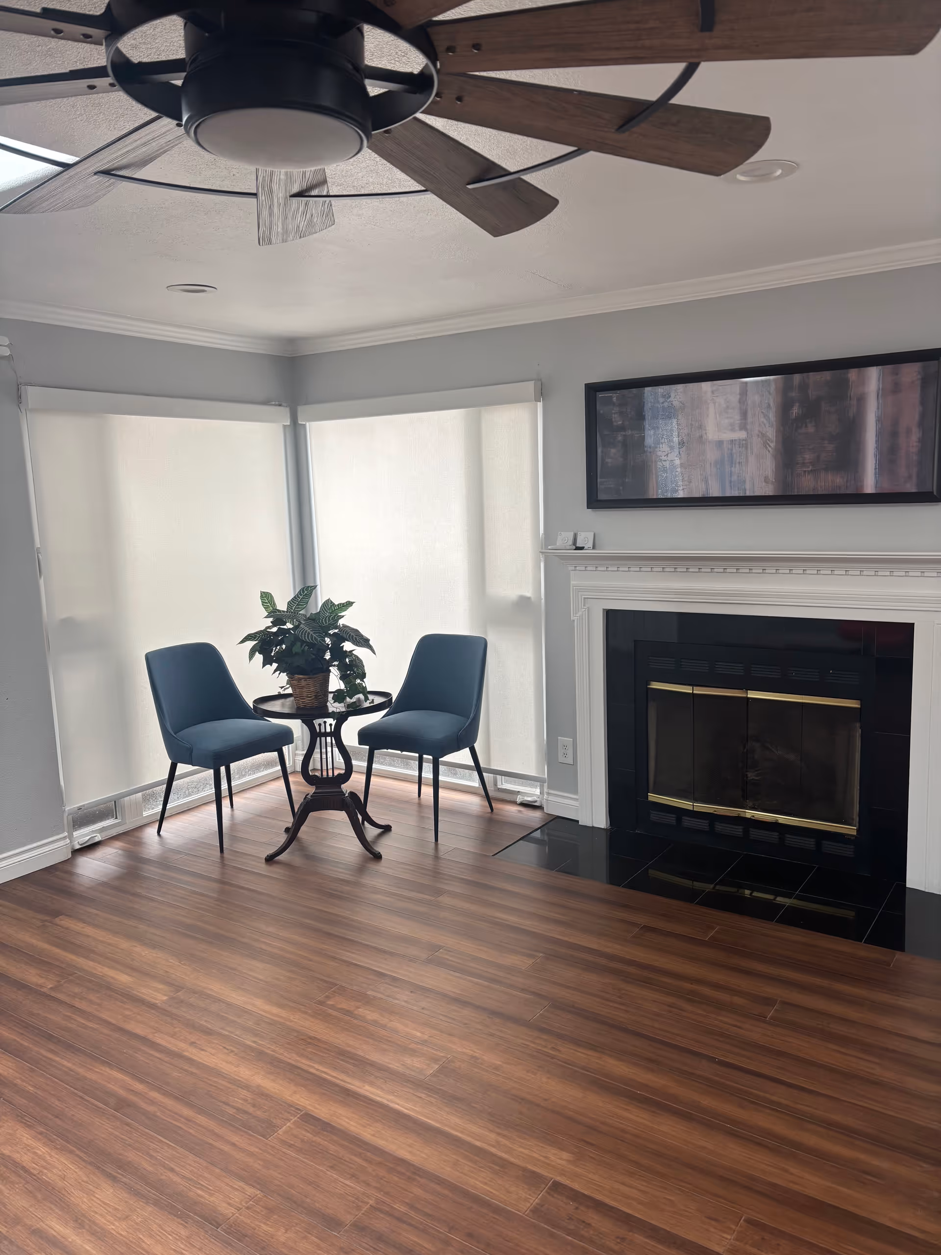 Cozy living room with two blue chairs, small table, plant, ceiling fan, and fireplace.