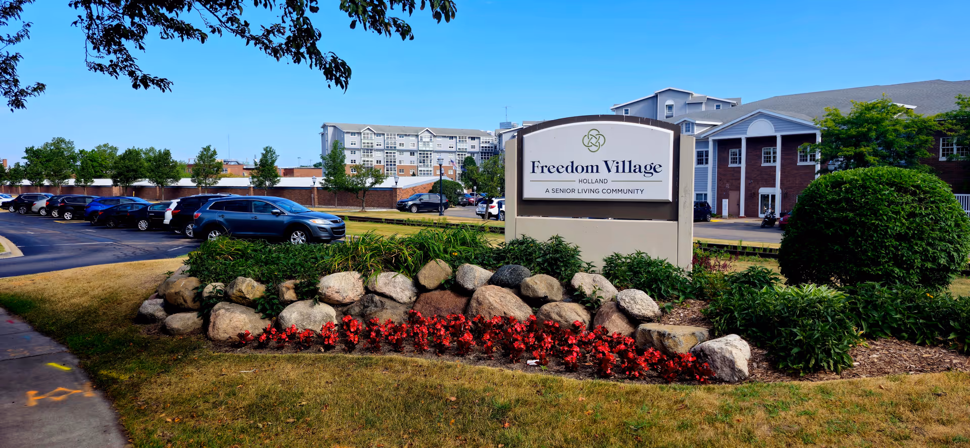 Front view of Freedom Village senior living facility sign with landscaped rocks and parking lot.
