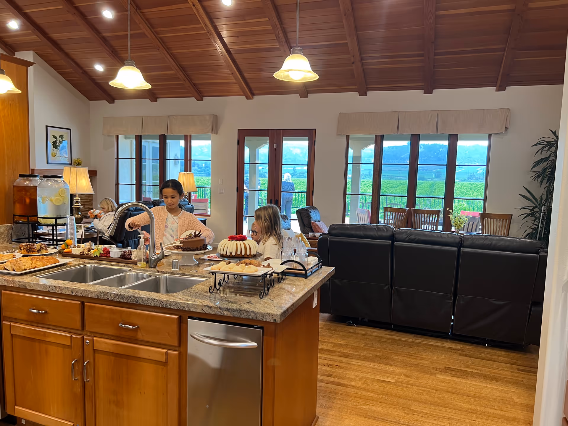 A communal kitchen island with pastries and drinks, residents seated nearby in a sunny common area.