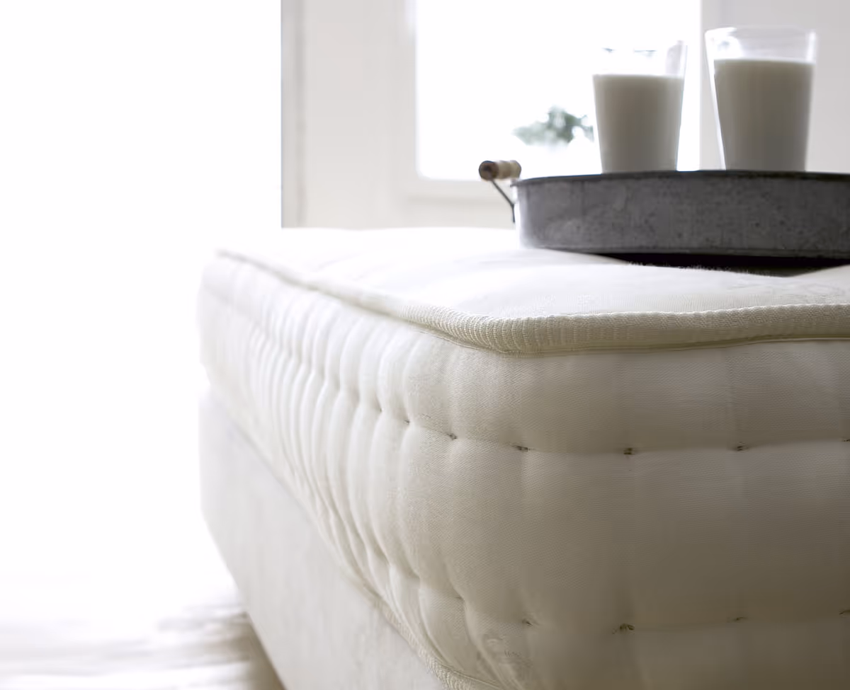 Close-up of a white tufted bed with a tray and two milk glasses by a window.