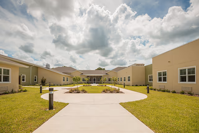 Sunny senior living facility exterior with a circular concrete path and landscaped courtyard.