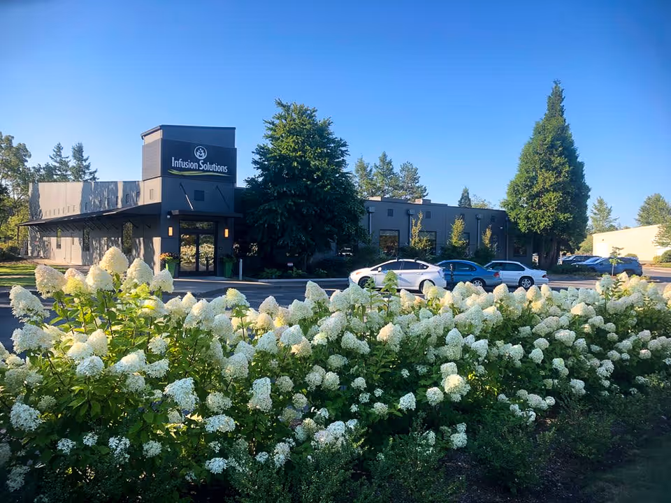 Exterior view of Infusion Solutions facility with flowering shrubs and parked cars.
