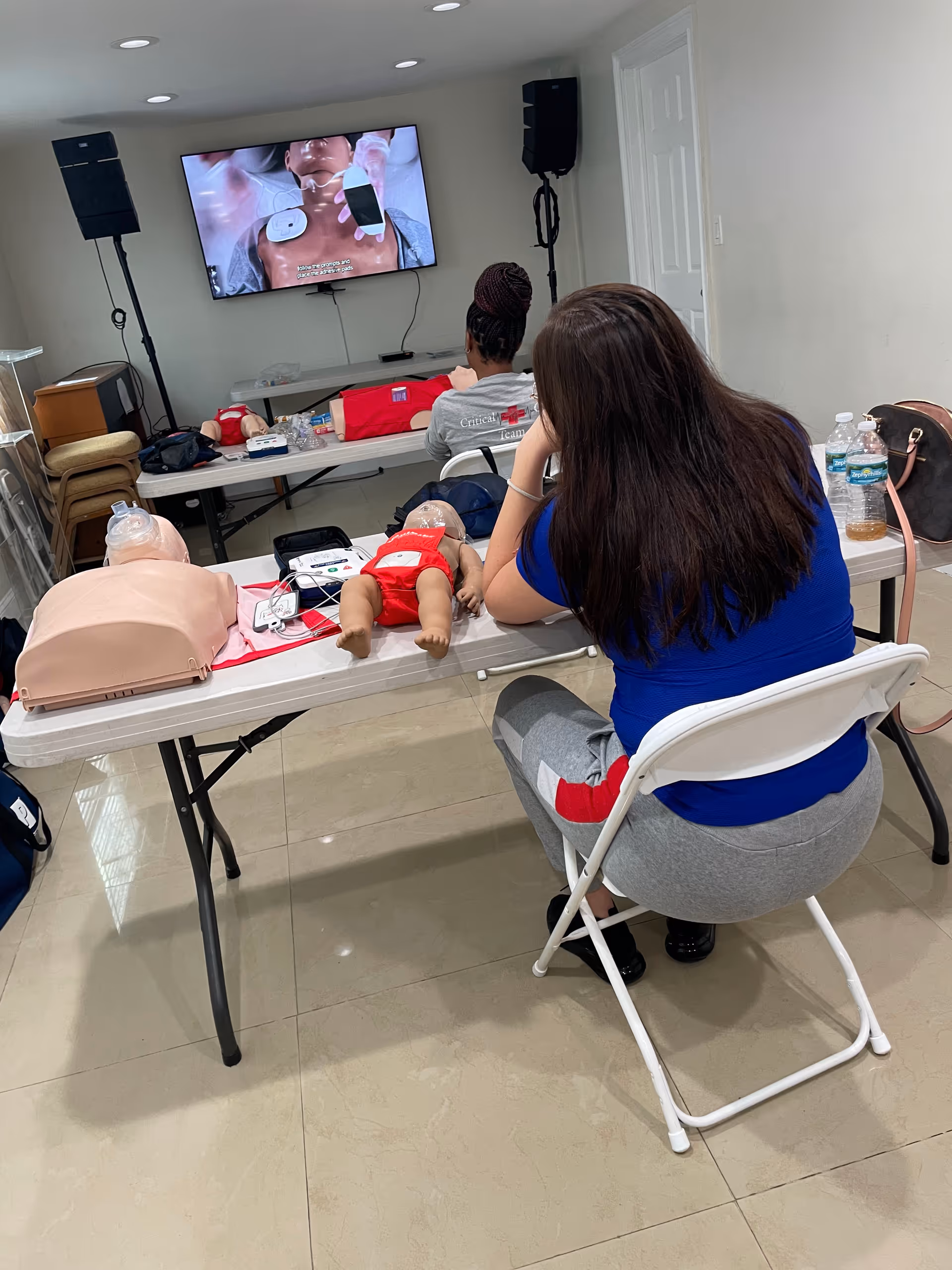 A training room in Kingdom Healthcare Services with CPR mannequins, a television, and a seated participant.