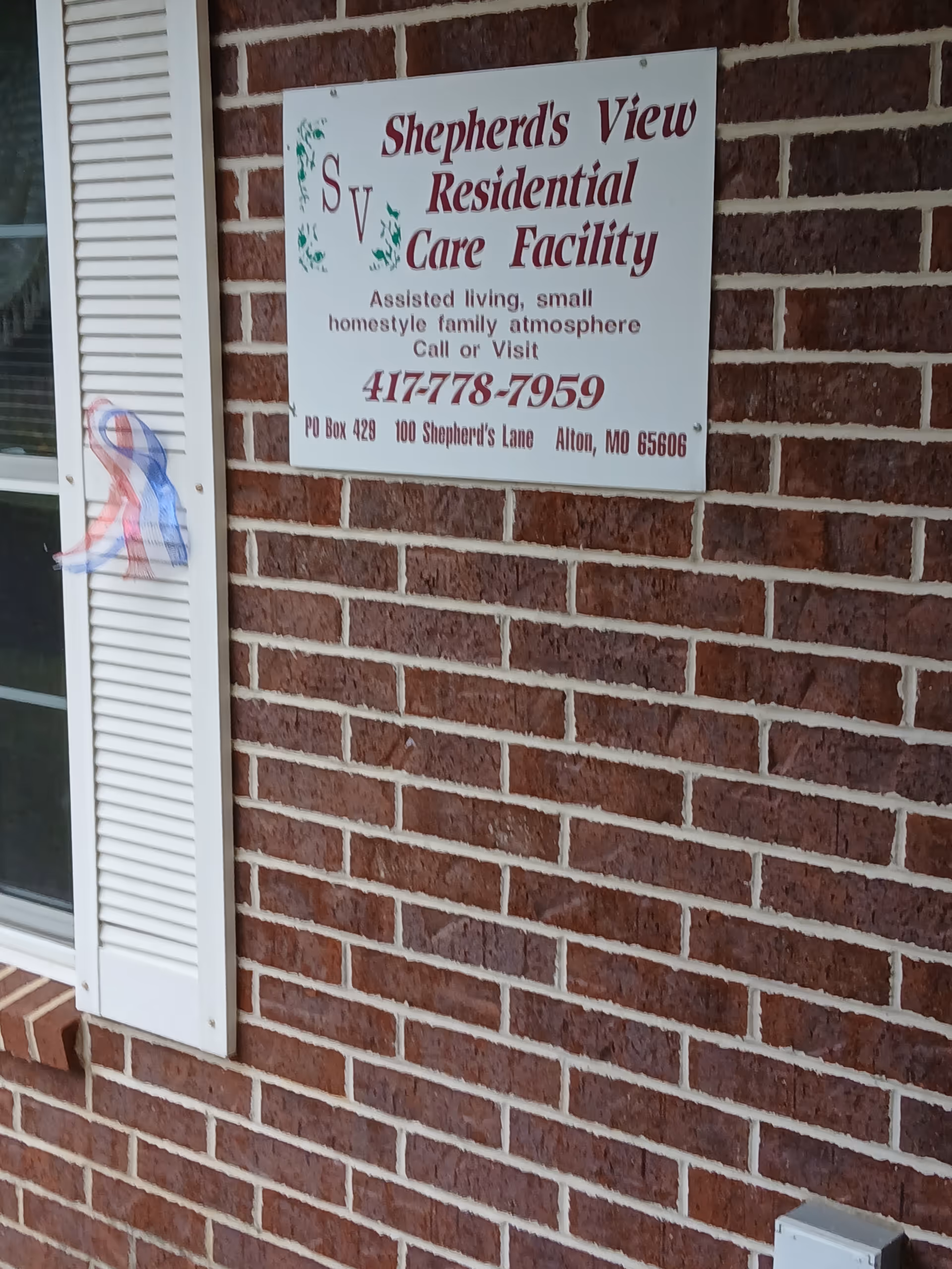 Brick exterior wall with a Shepherds View Residential Care Facility sign beside a window.