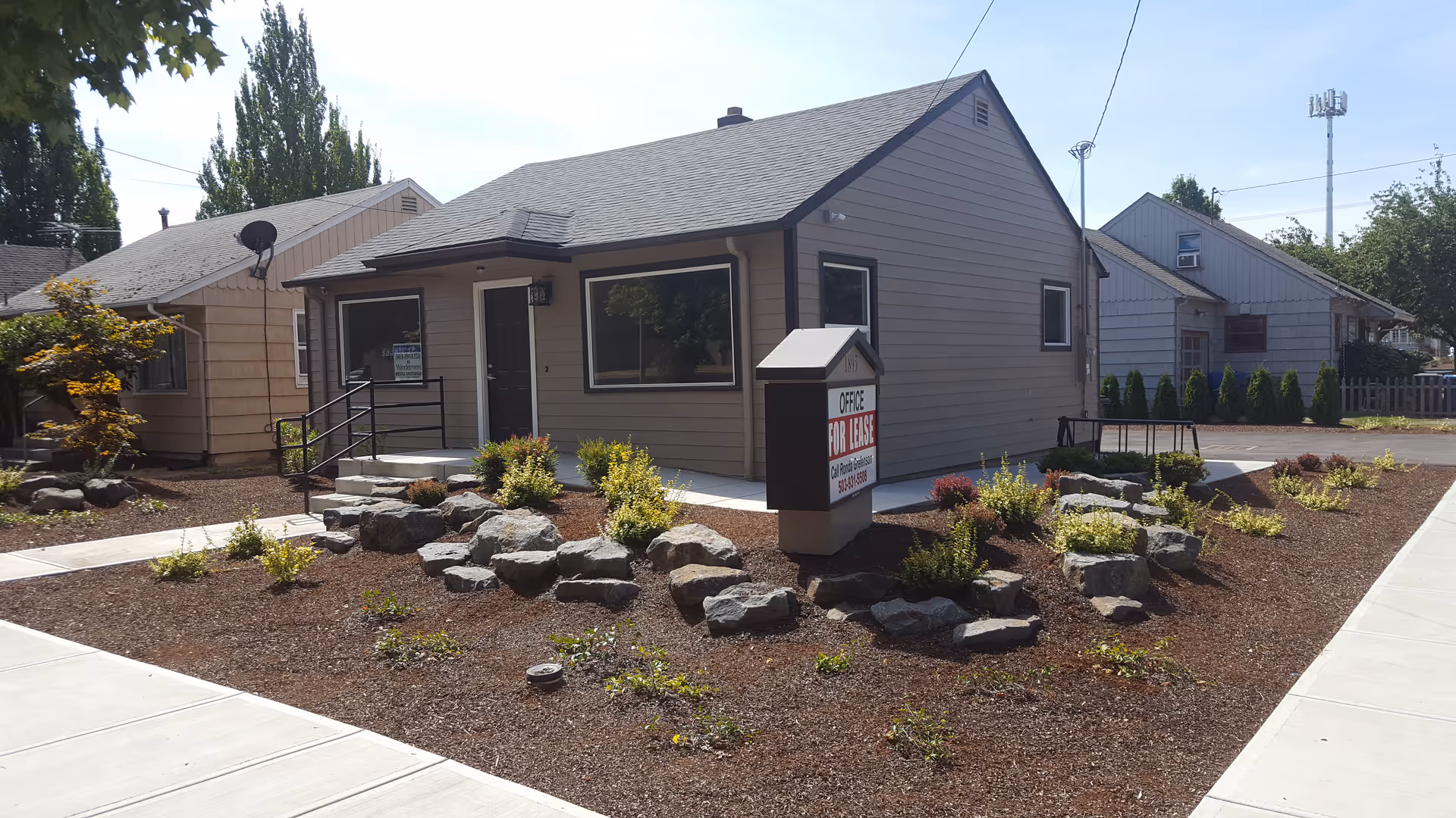 Small beige office building with rock garden landscaping and an Office For Lease sign.