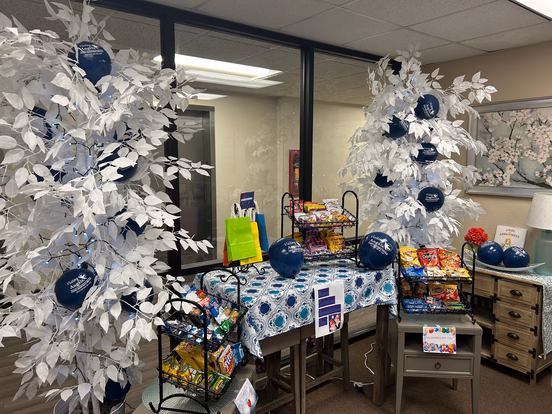 Indoor display of snacks and decorative white trees with blue balloons in a facility lobby.