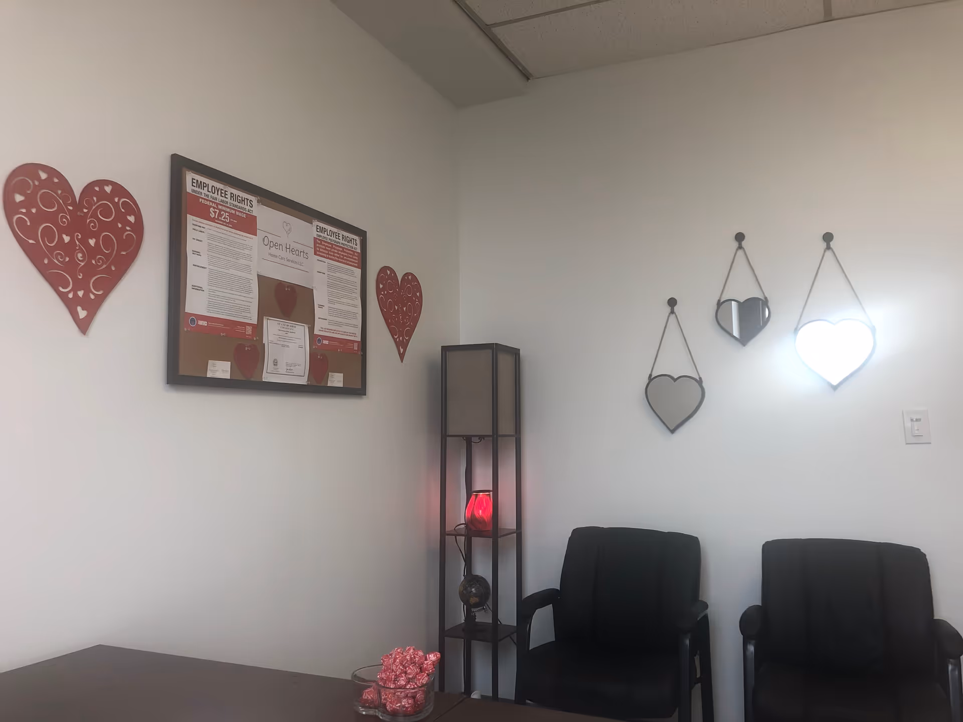 Interior waiting area with black chairs, heart decor, and bulletin board on white wall.