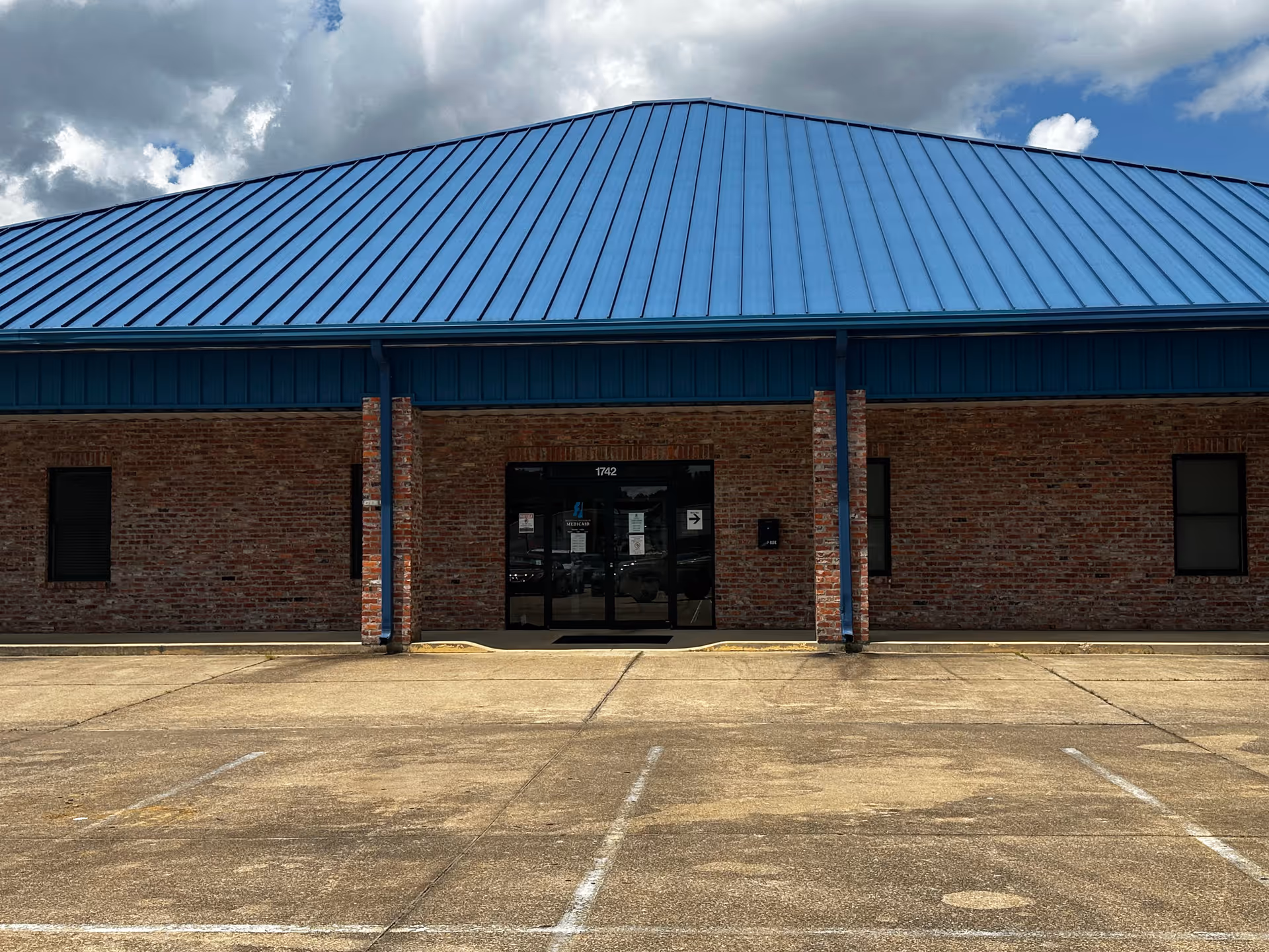 Brick building with a blue metal roof and a centered glass entrance.