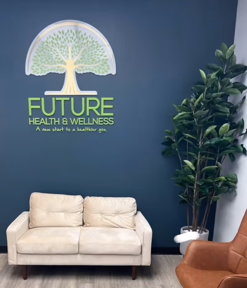 Blue wall with Future Health & Wellness logo, cream couch, and tall plant in the lobby.