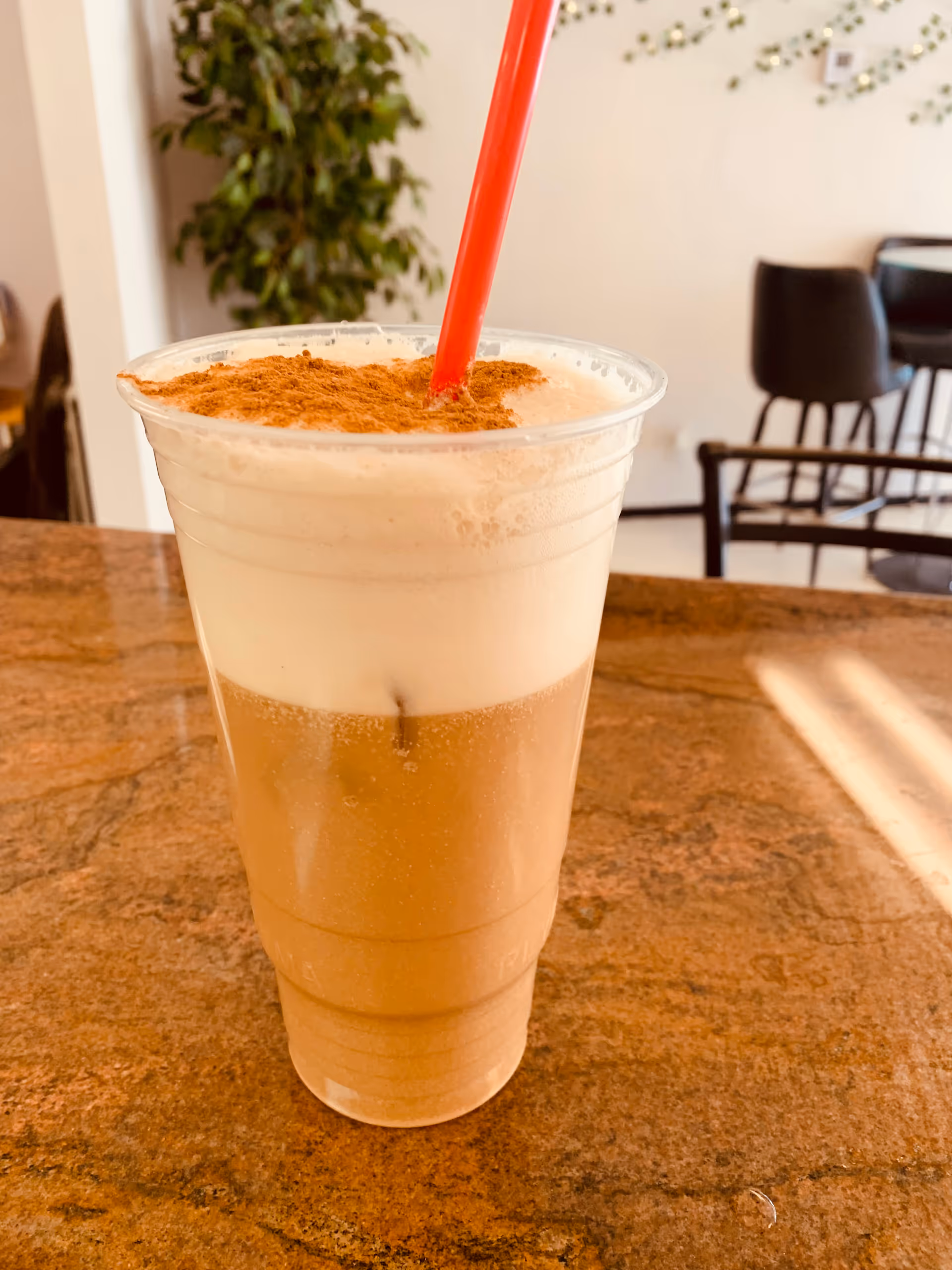 Iced coffee drink with whipped cream and cinnamon on a brown countertop indoors.