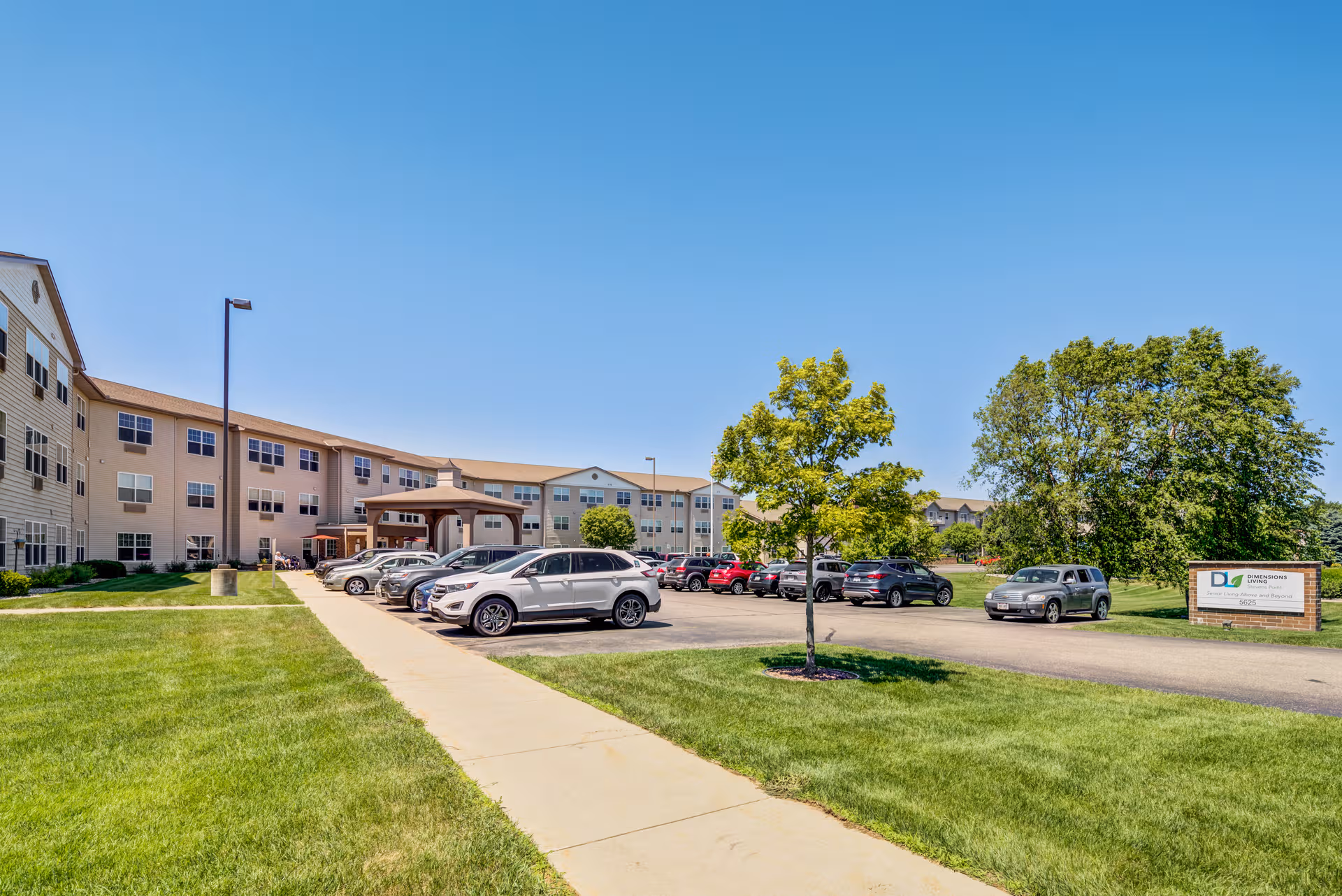 Exterior view of Dimensions Living Stevens Point facility with a parking lot, sign, and green lawn.