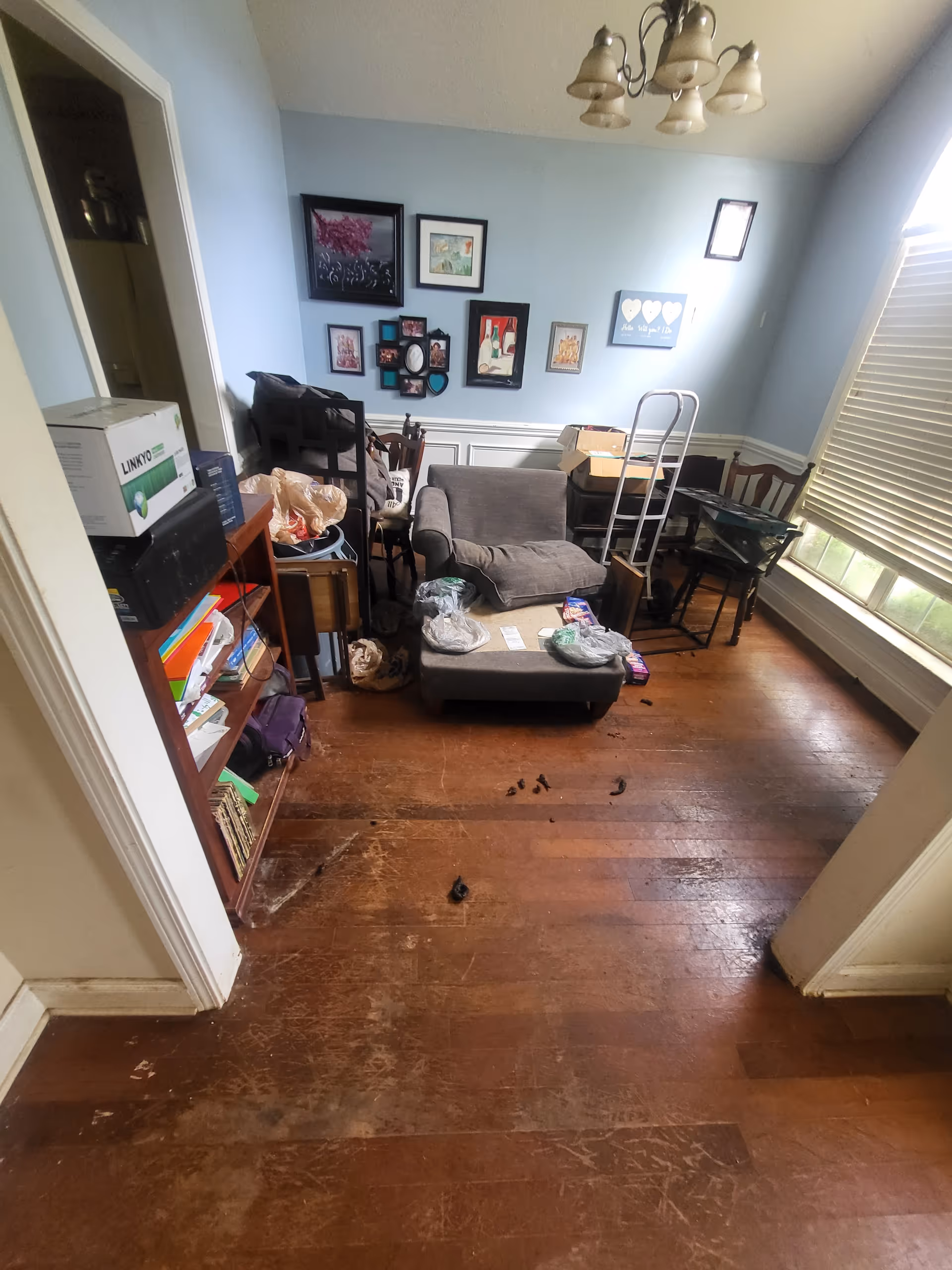 A cluttered living room with couches, chairs, and scattered items in a sunny facility space.