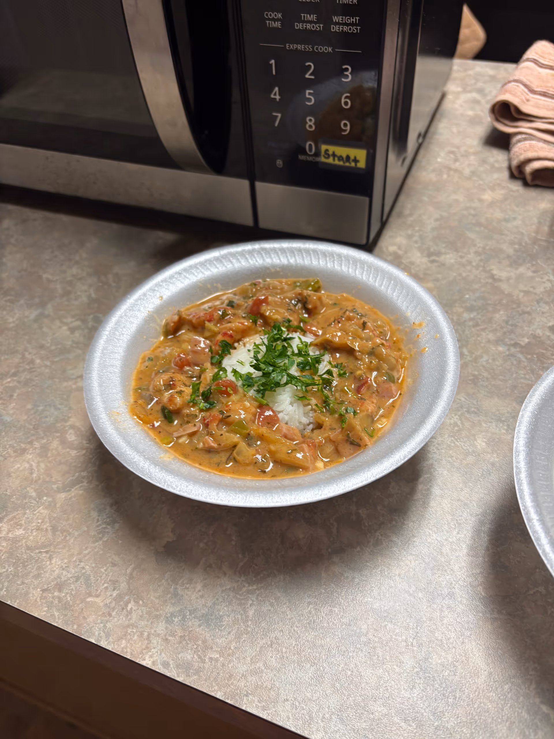 A bowl of stew with rice and herbs on a kitchen counter near a microwave.