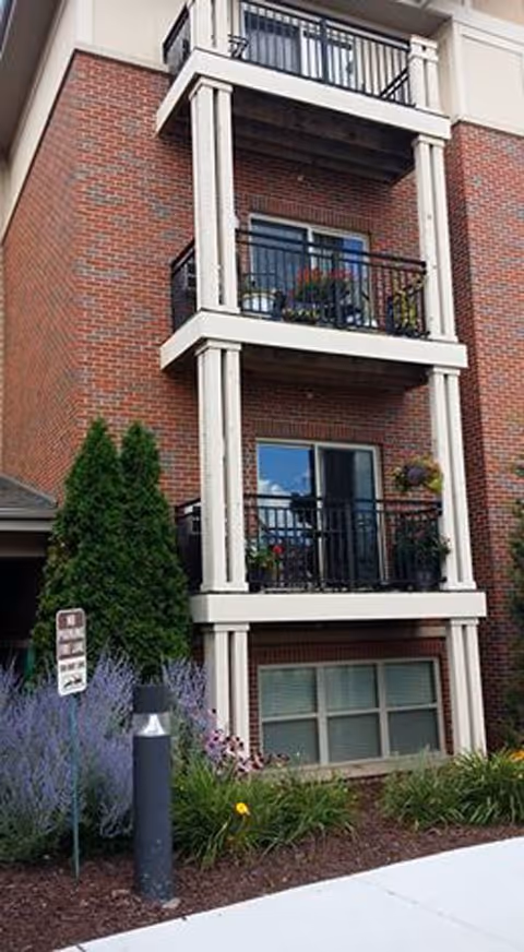 Exterior brick senior living building with three balconies and landscaped ground-floor area.