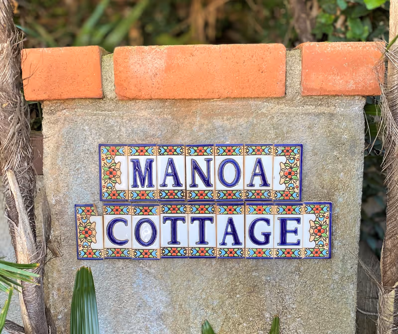 Stone pillar bearing a decorative MANOA COTTAGE sign at entrance.