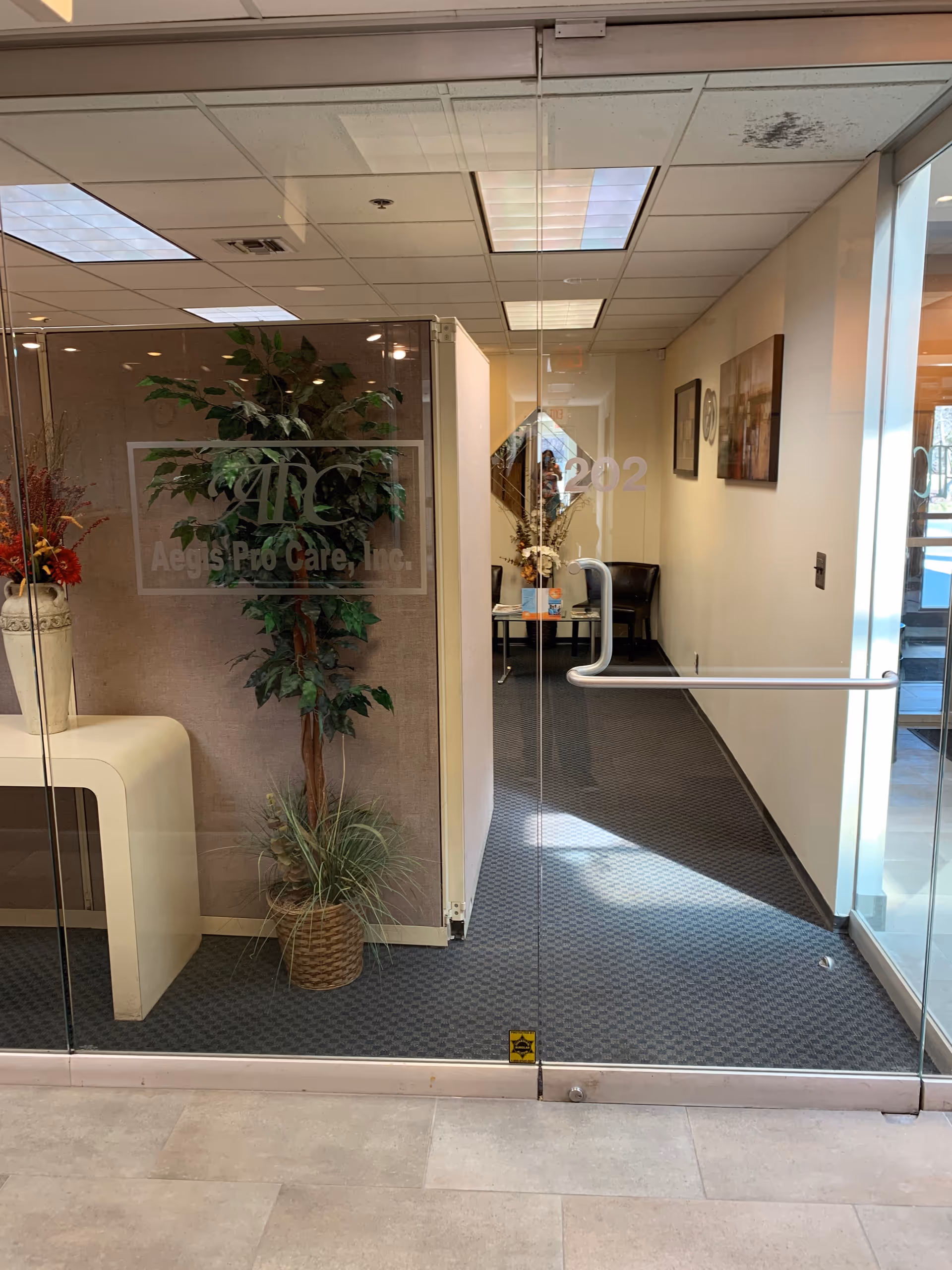 Lobby interior of Aegis Pro Care Inc featuring glass doors, potted plants, and a hallway.