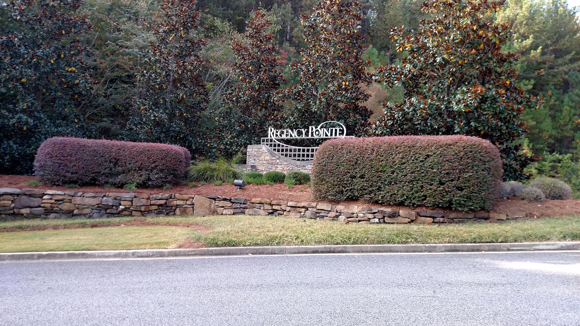 Entrance sign reading Regency Pointe amid trimmed hedges and a stone retaining wall.