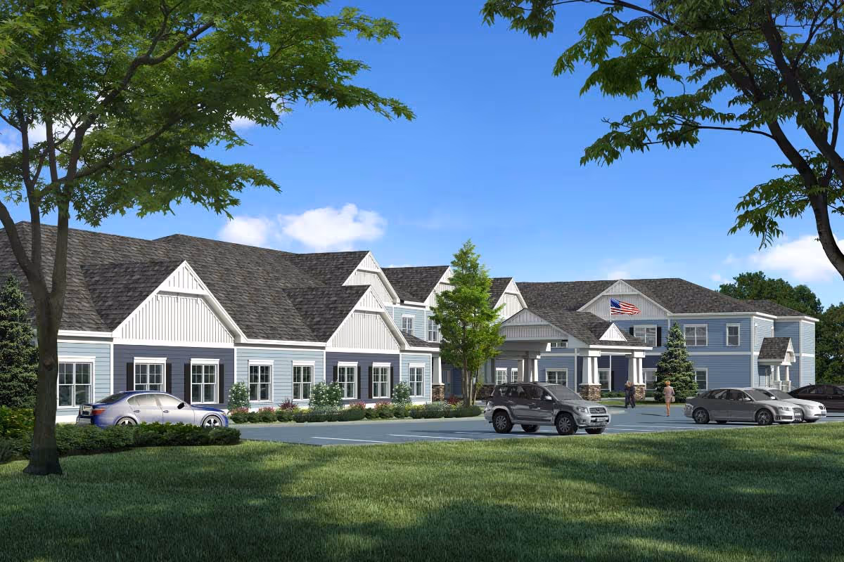Front exterior of a two-story senior living building with a covered entrance, parked cars, trees, and a manicured lawn under a blue sky.