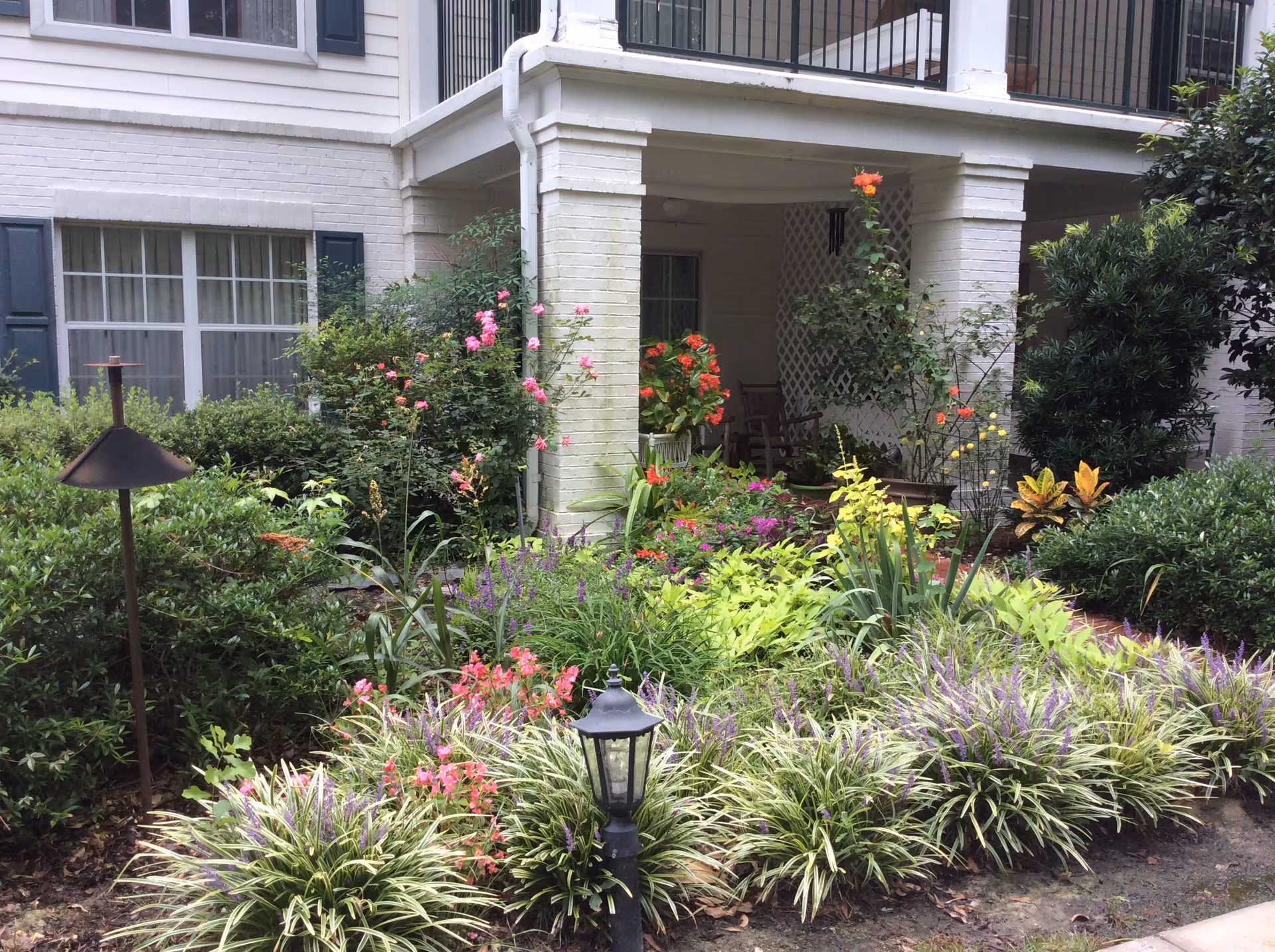 A white brick building with a covered porch and vibrant flower garden in front.