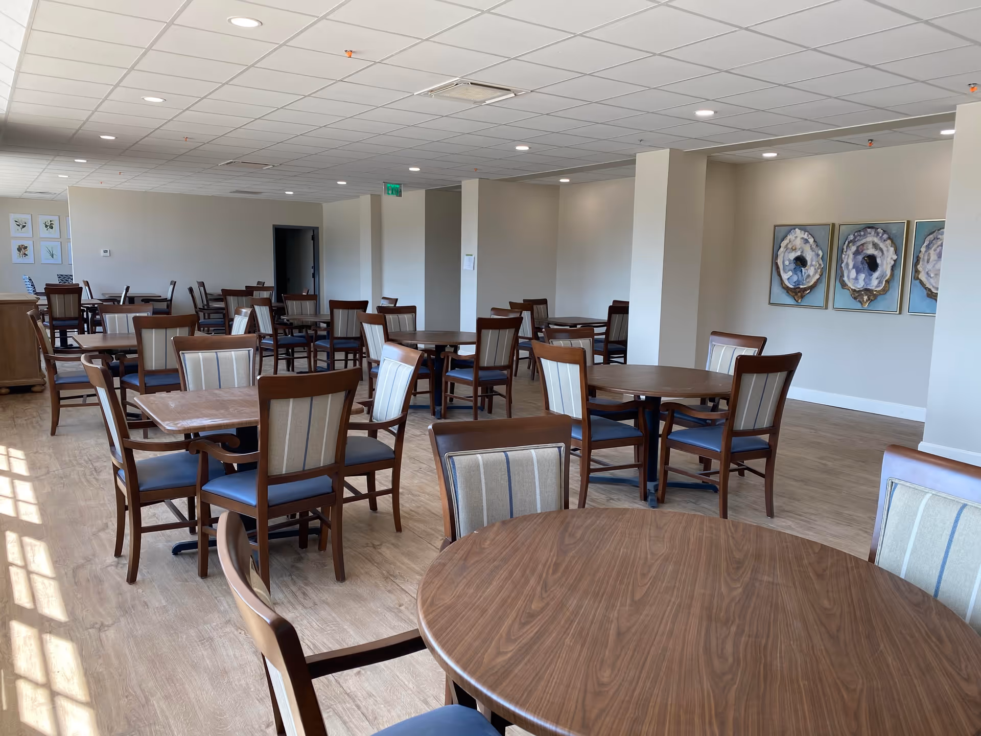Spacious dining room with multiple wooden tables and upholstered chairs and wall art.