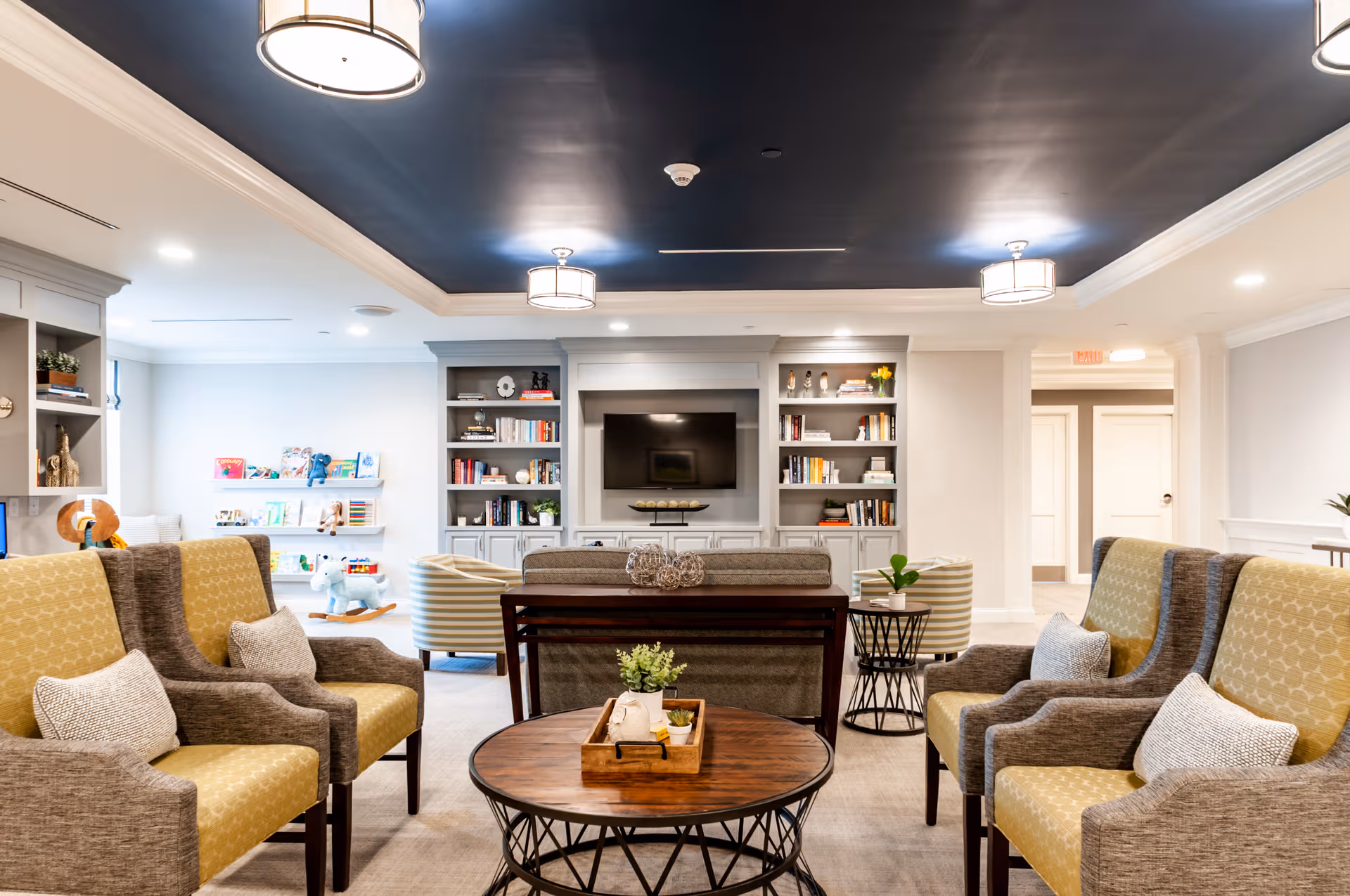 Spacious, modern senior living lounge with seating, coffee tables, and a central TV.