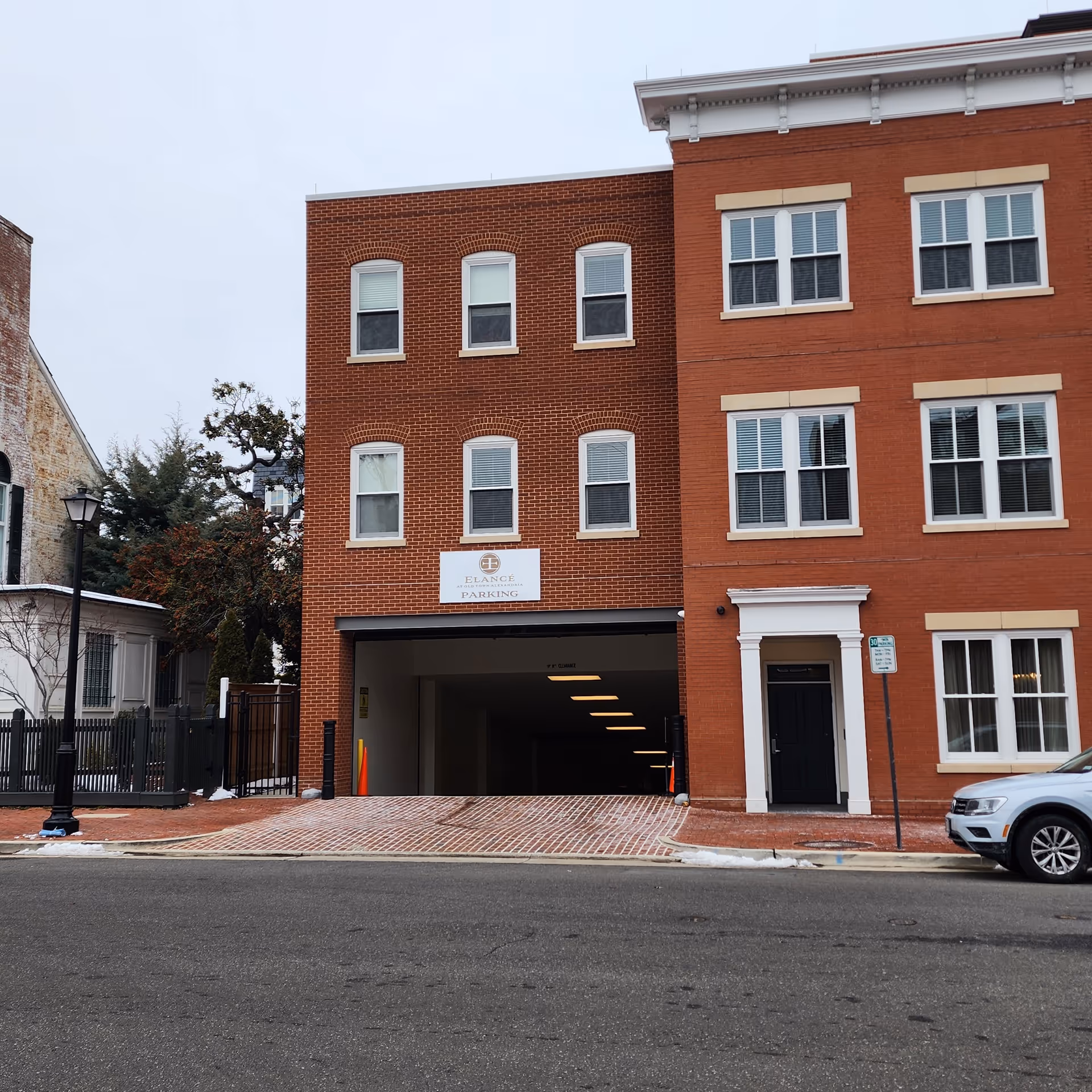 Brick three-story building with a wide open garage entrance and a parked car.