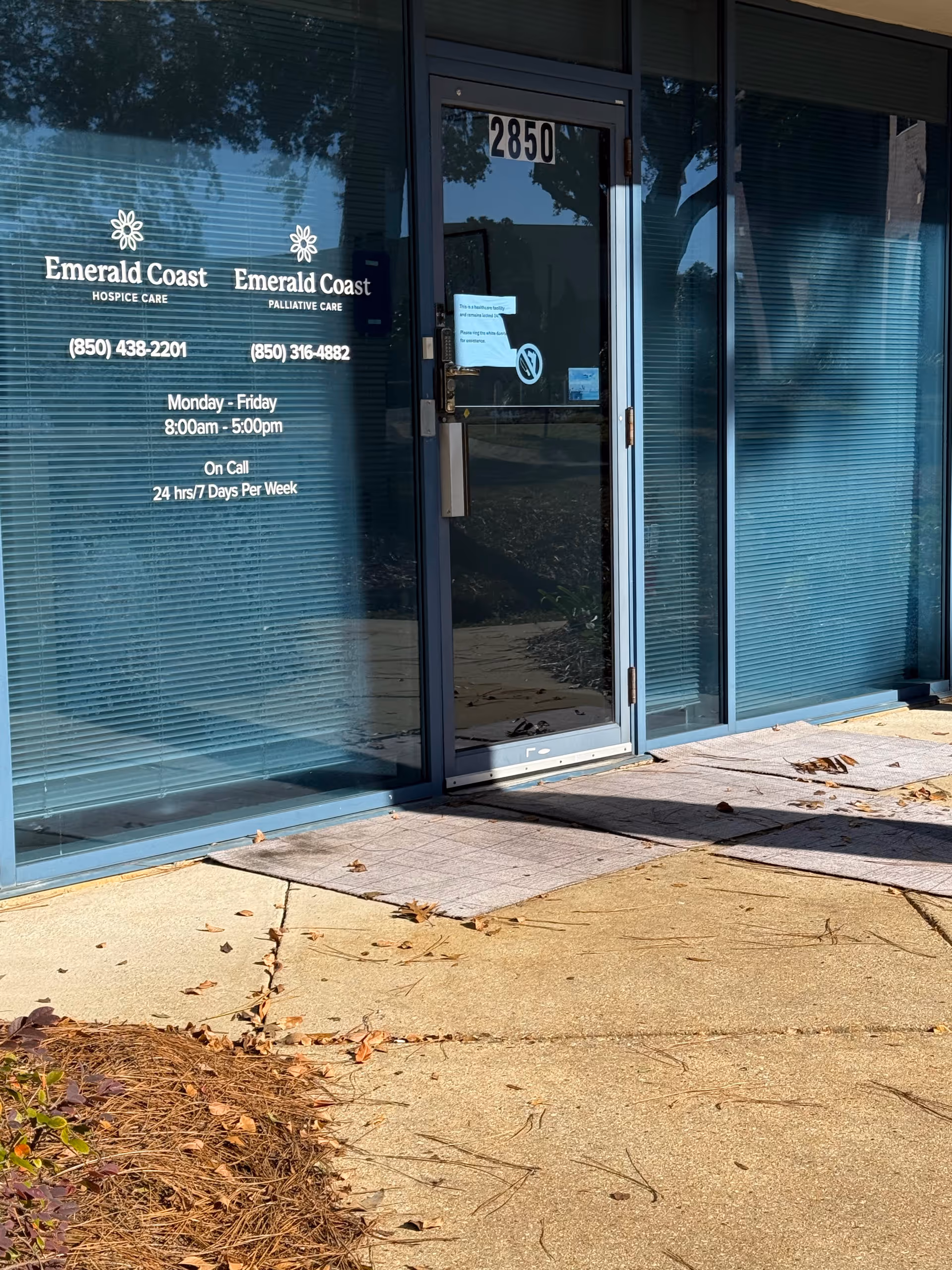 Glass storefront entrance of Emerald Coast Hospice at 2850, with signage and blue blinds.