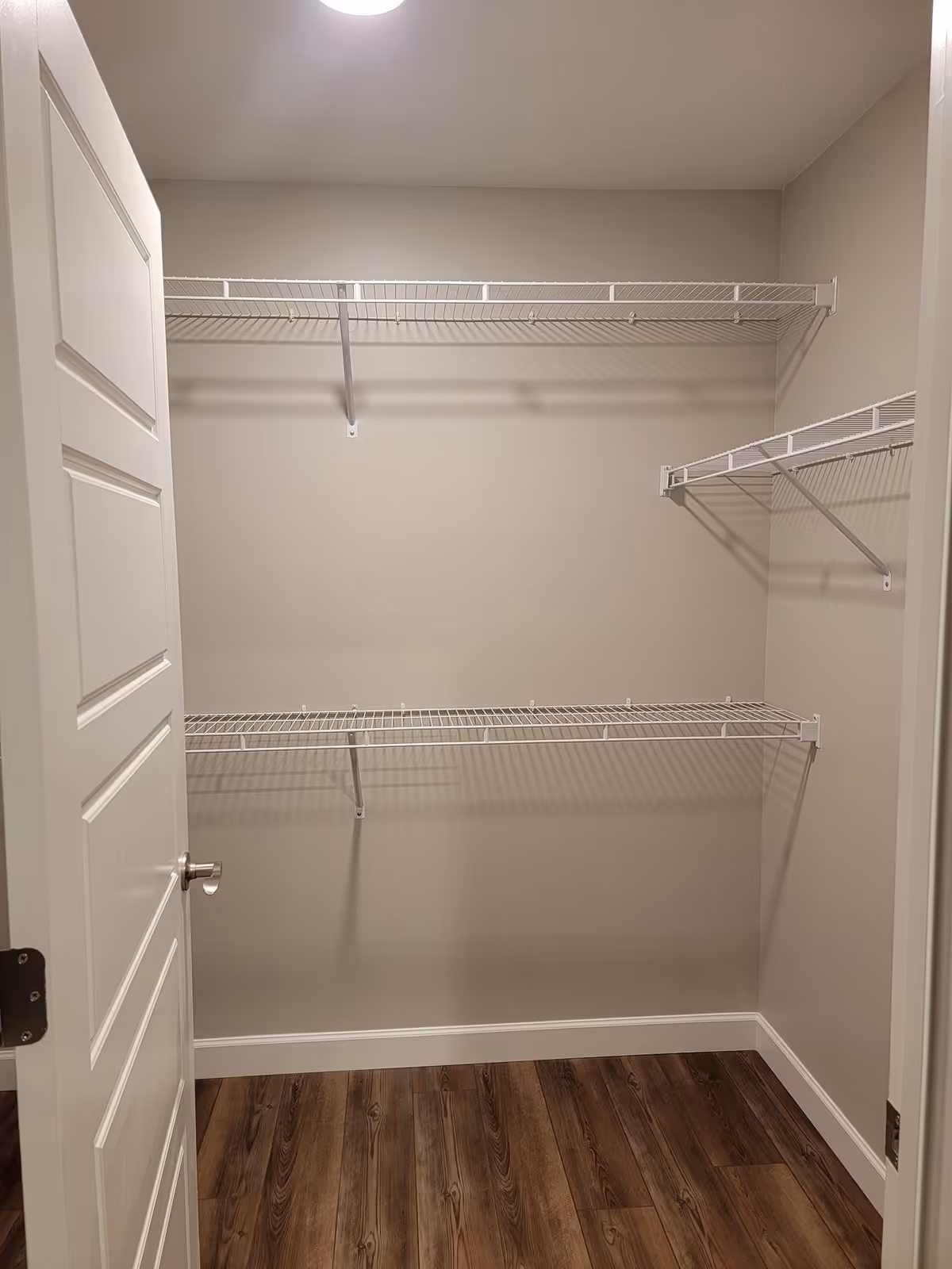 Open closet with white wire shelves and wood-look laminate flooring.