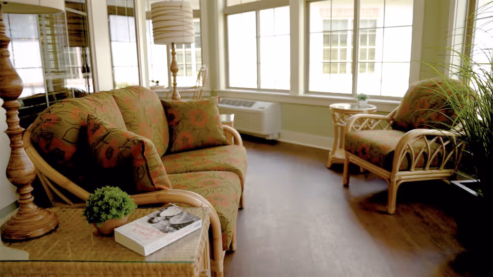 Bright lounge with floral-patterned wicker seating, a coffee table, and large windows.