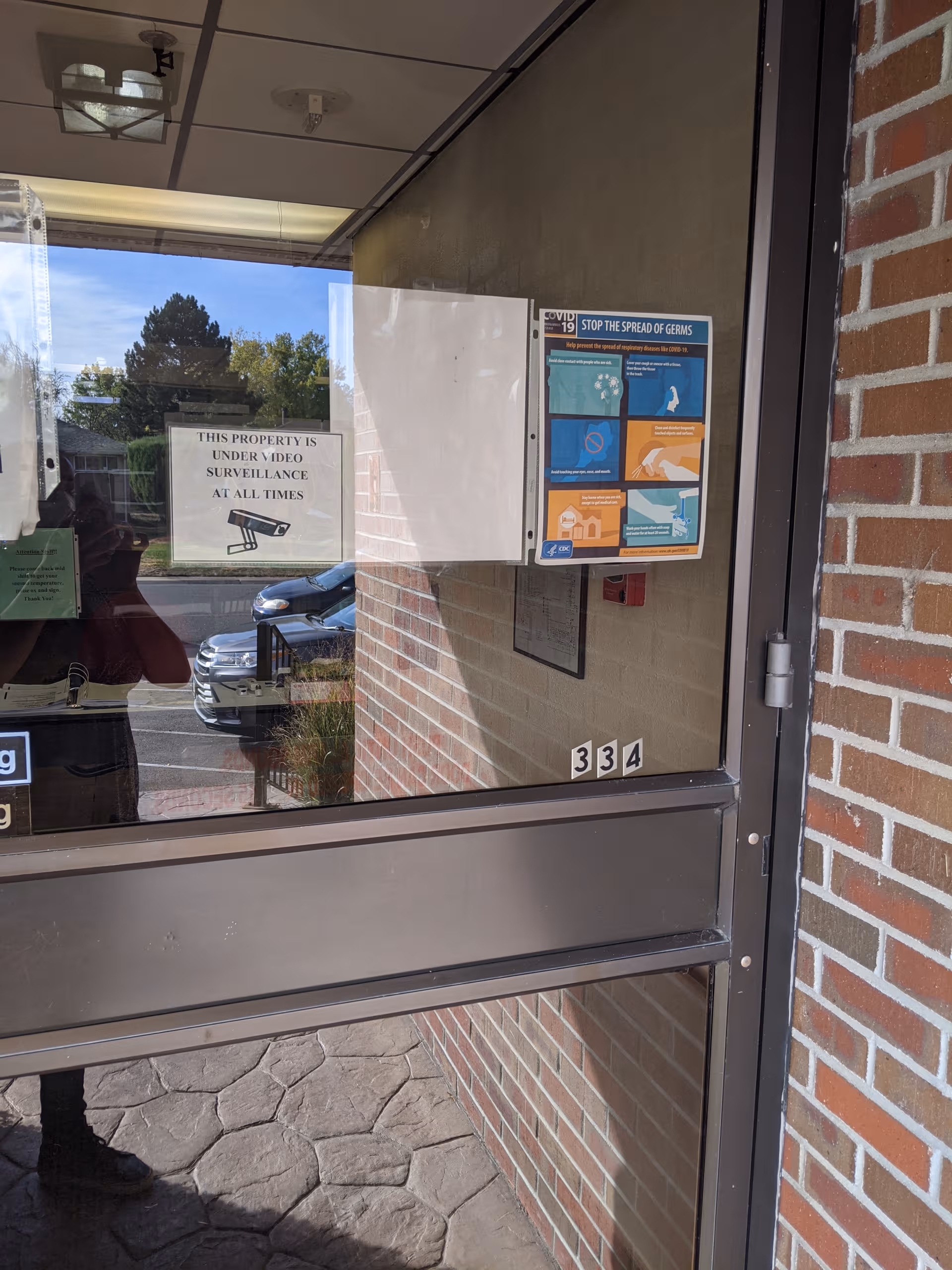 Glass entry door with notices, brick exterior, and a parked car visible outside the facility.
