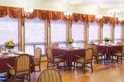 Empty dining room with round tables, chairs, and burgundy tablecloths by windows.