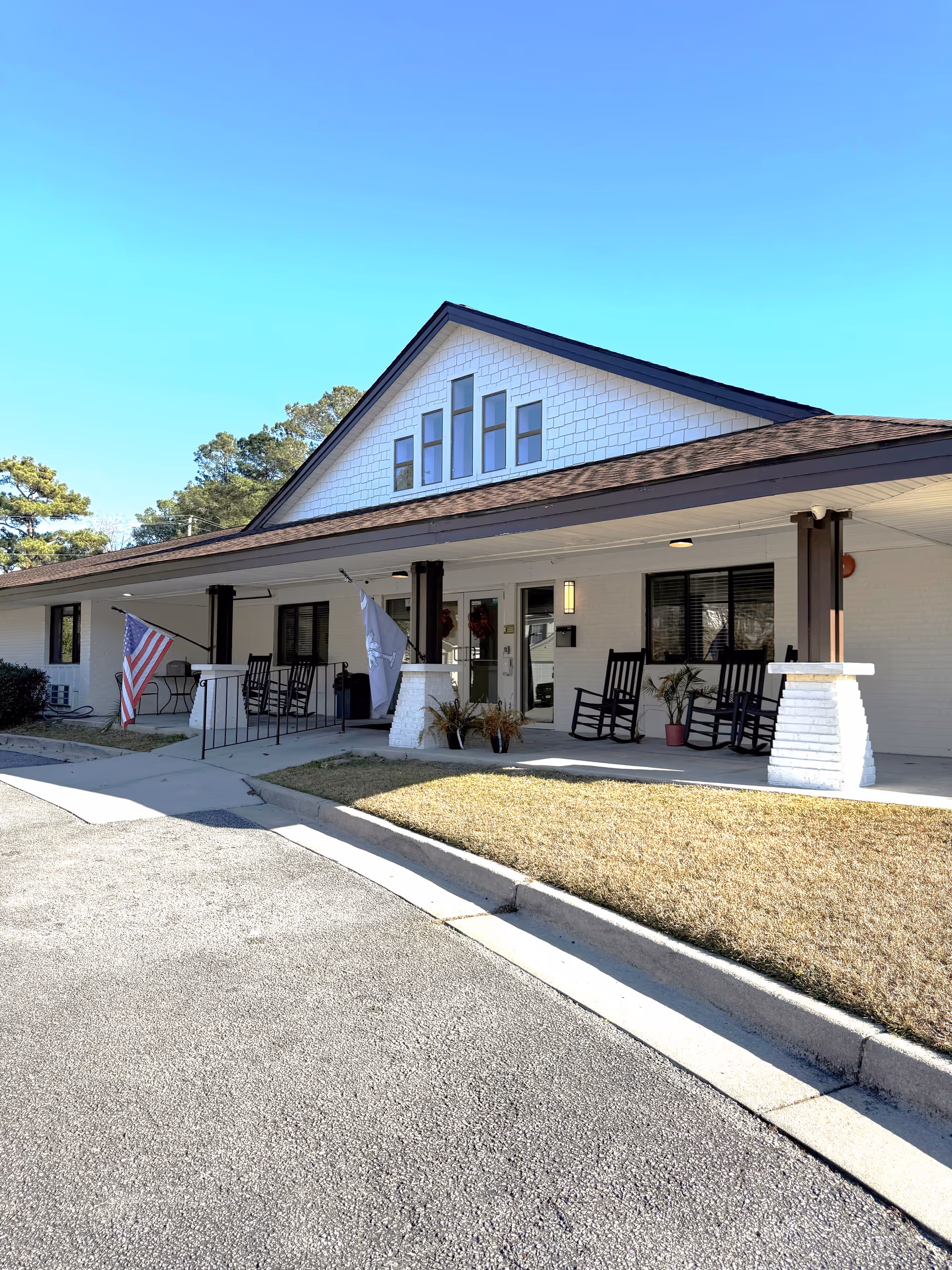 Front view of The Marsh at North Charleston, white brick senior living facility with rocking chairs.