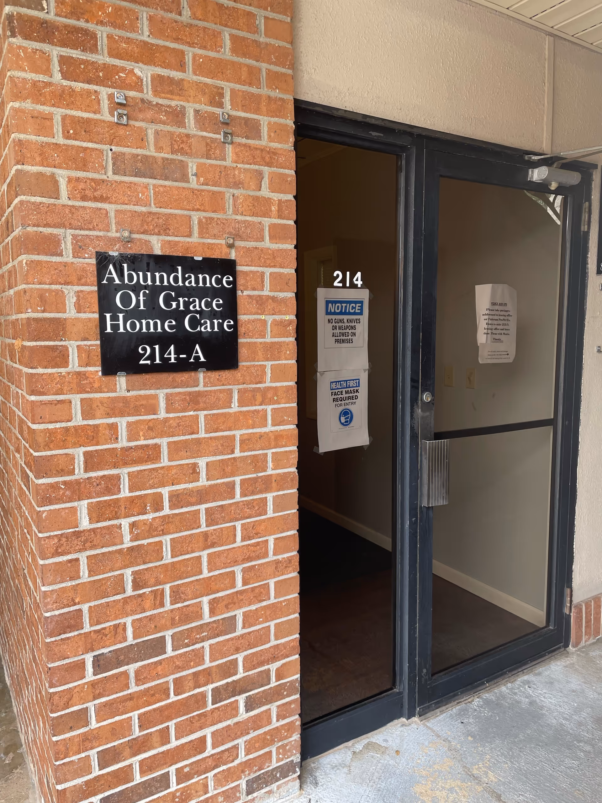 Brick exterior with Abundance Of Grace Home Care sign beside an open doorway.
